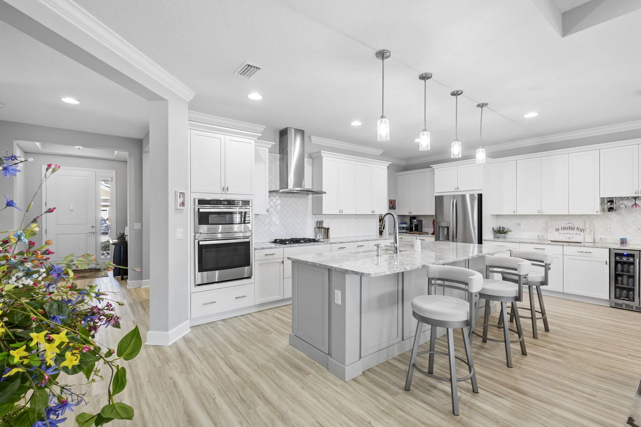Modern kitchen with white cabinets, stainless steel appliances, marble island, pendant lighting, and light wood flooring.