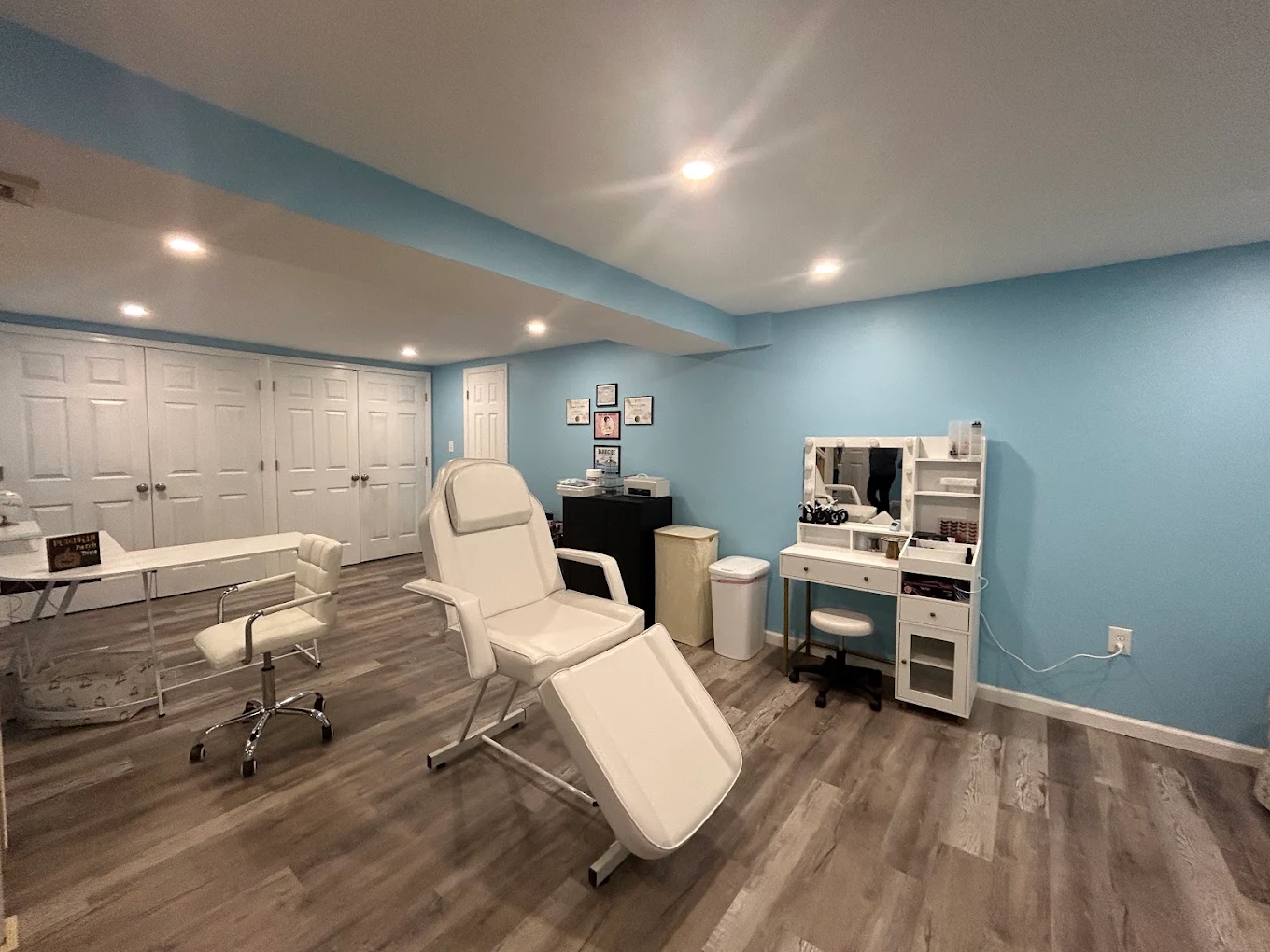 Medical or spa treatment room with a reclining chair, white swivel chair, small desk, and blue walls.