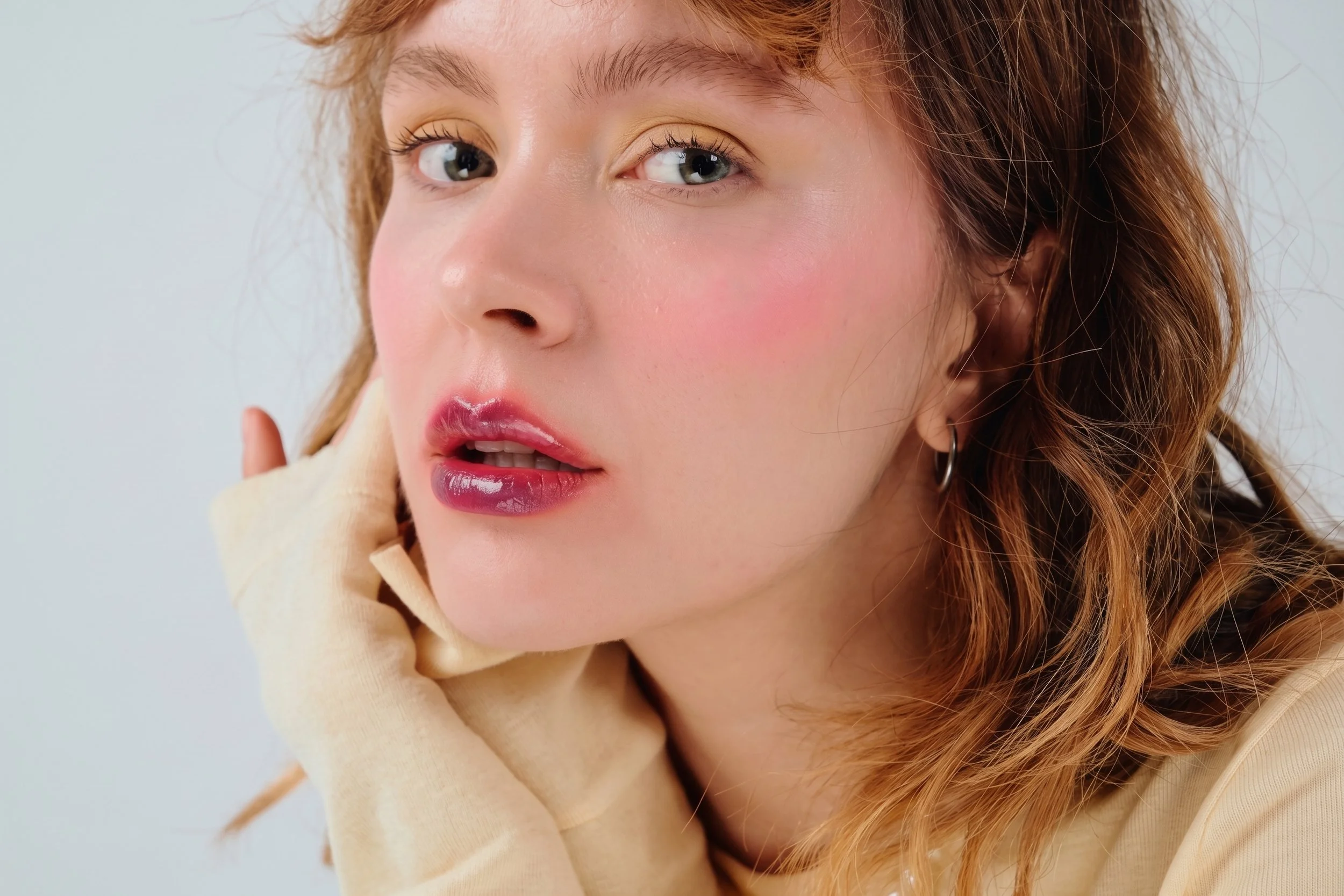 Portrait d'une jeune femme avec des cheveux roux, portant un maquillage léger, avec un fond neutre.