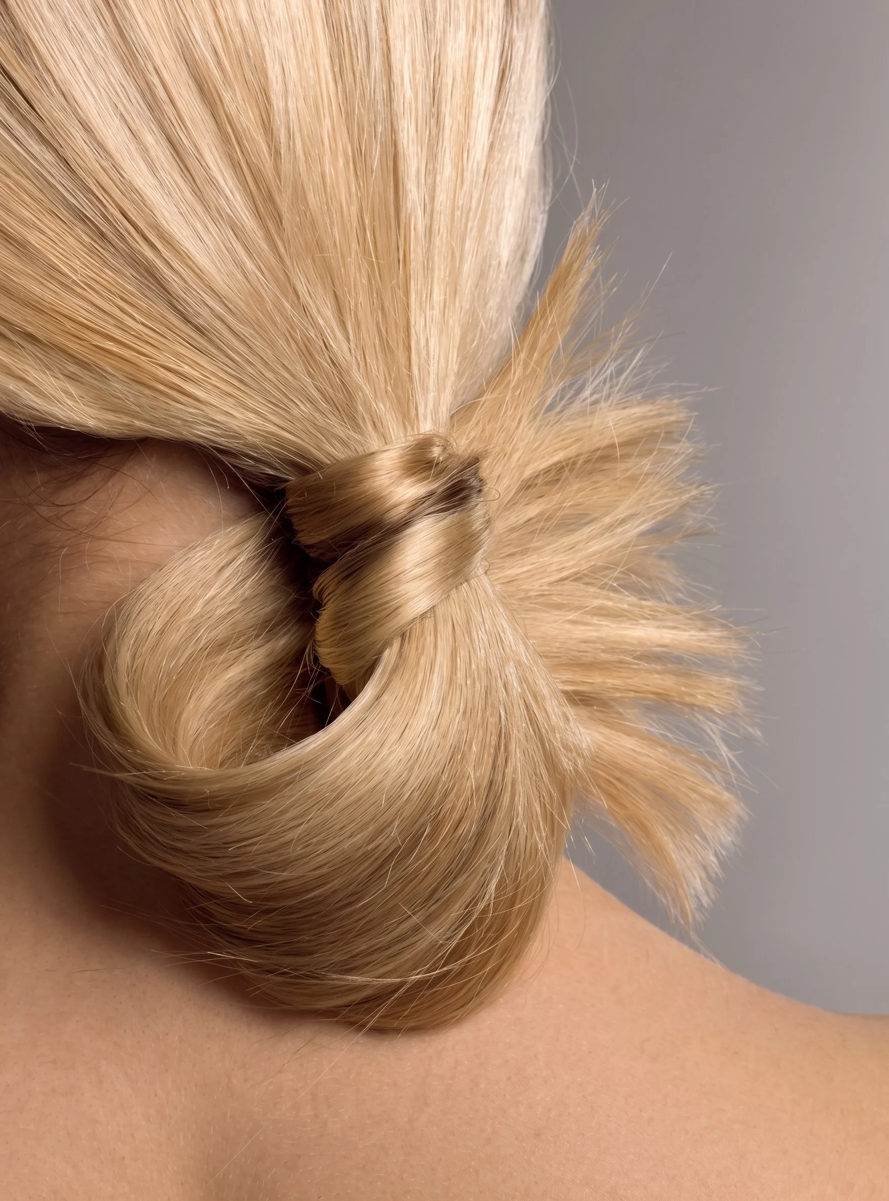 Cheveux blonds coiffés en boucle, porté sur une épaule nue avec la peau visible.