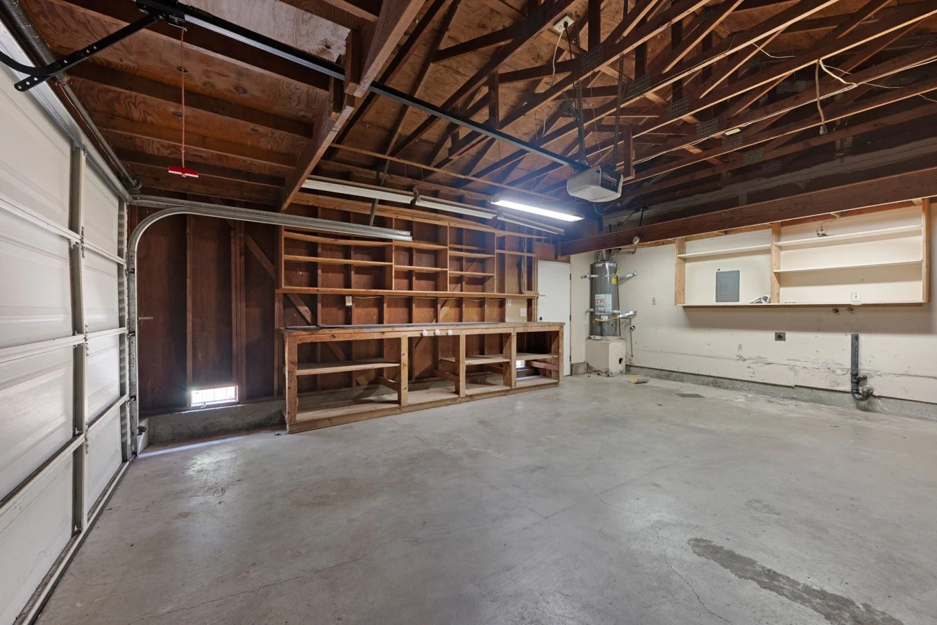 Empty garage with wooden shelves, a garage door, and an unfinished wall with some plumbing.