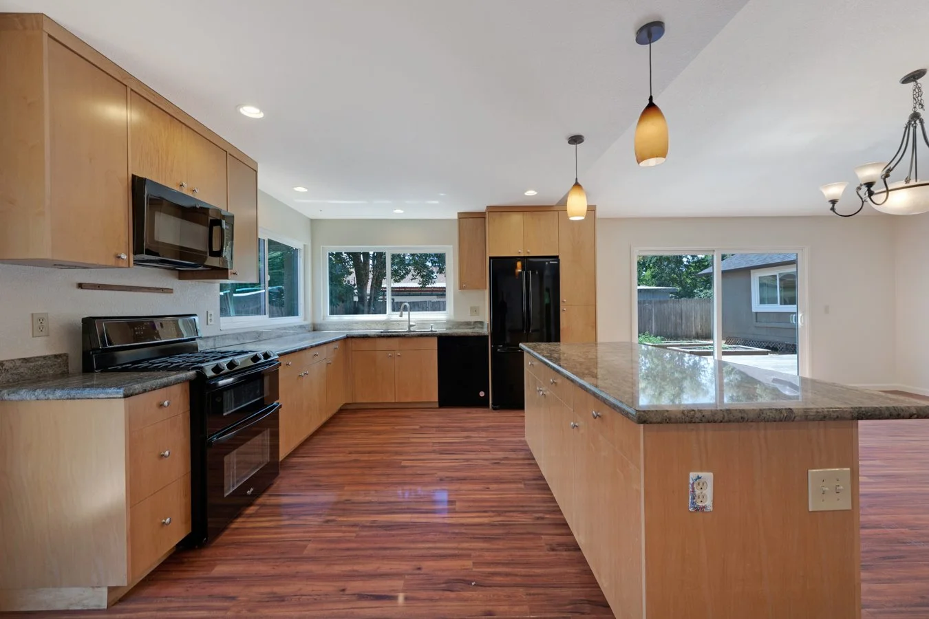 Modern kitchen with wooden cabinets, stainless steel appliances, granite countertops, hardwood floors, large windows, and pendant lights.