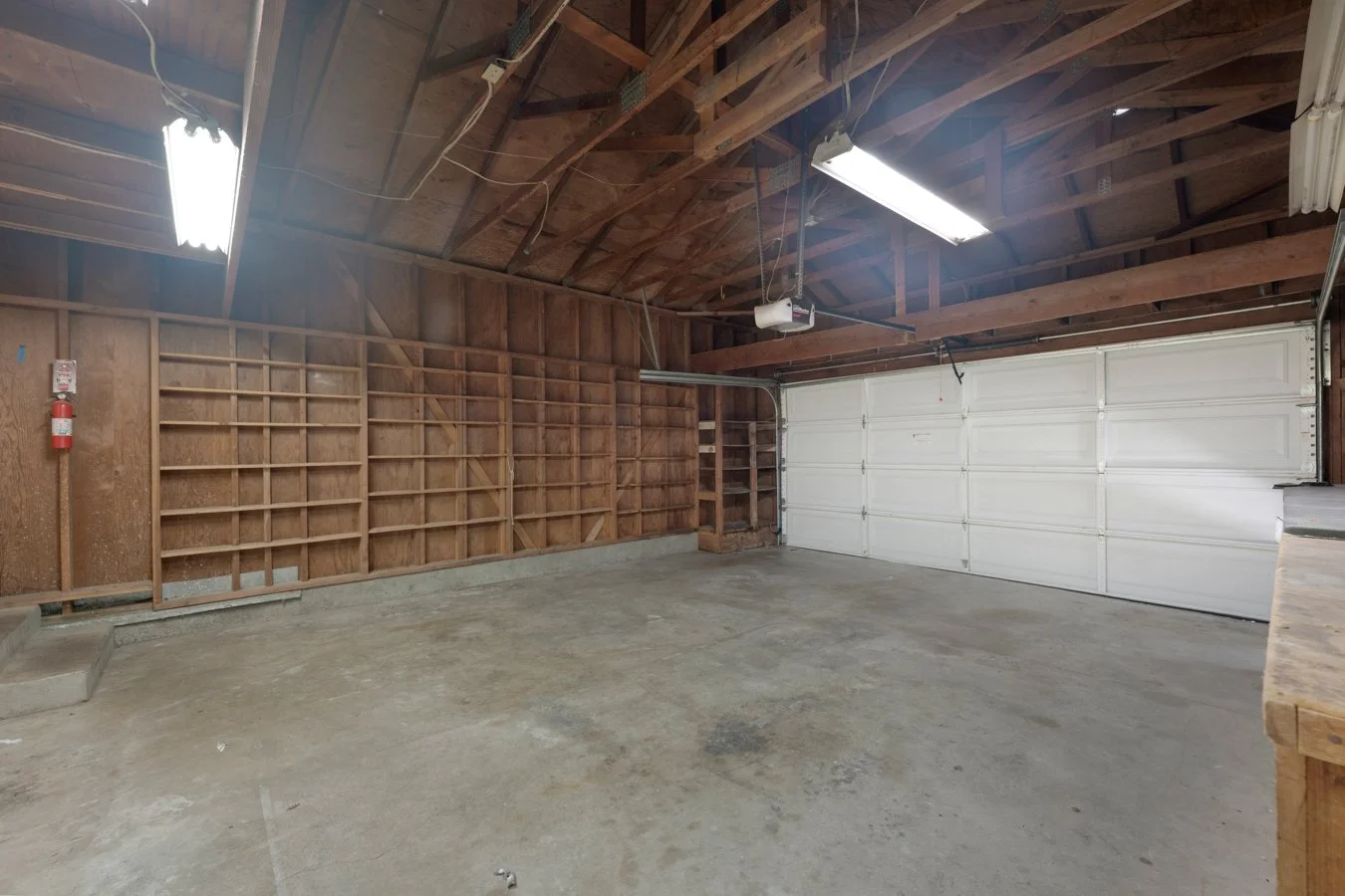 Empty garage with concrete floor, wooden walls, and a white roll-up garage door.