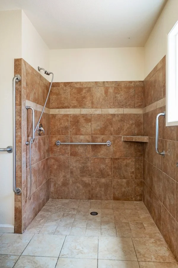 Accessible shower with brown tiles, safety grab bars, a small corner shelf, and a window.