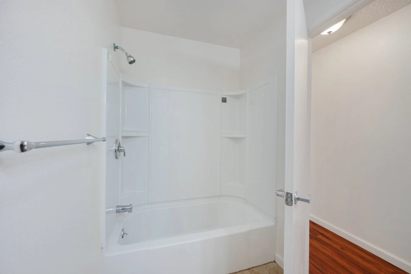 Empty white bathtub with showerhead, soap dish, and towel bars in a bathroom.