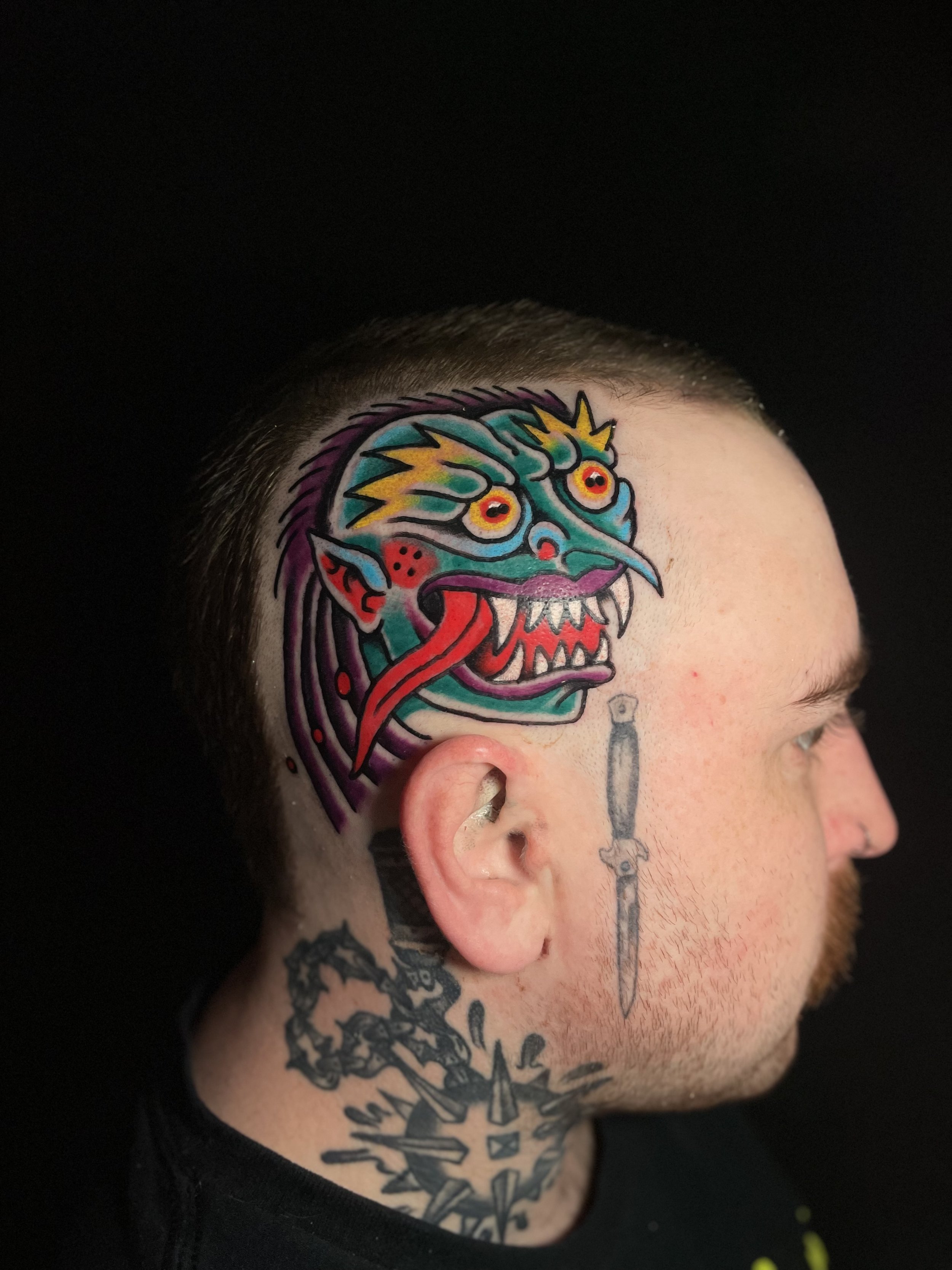 Colorful tattoo of a dragon's face with yellow, blue, purple, red, and black details on person's head and neck.