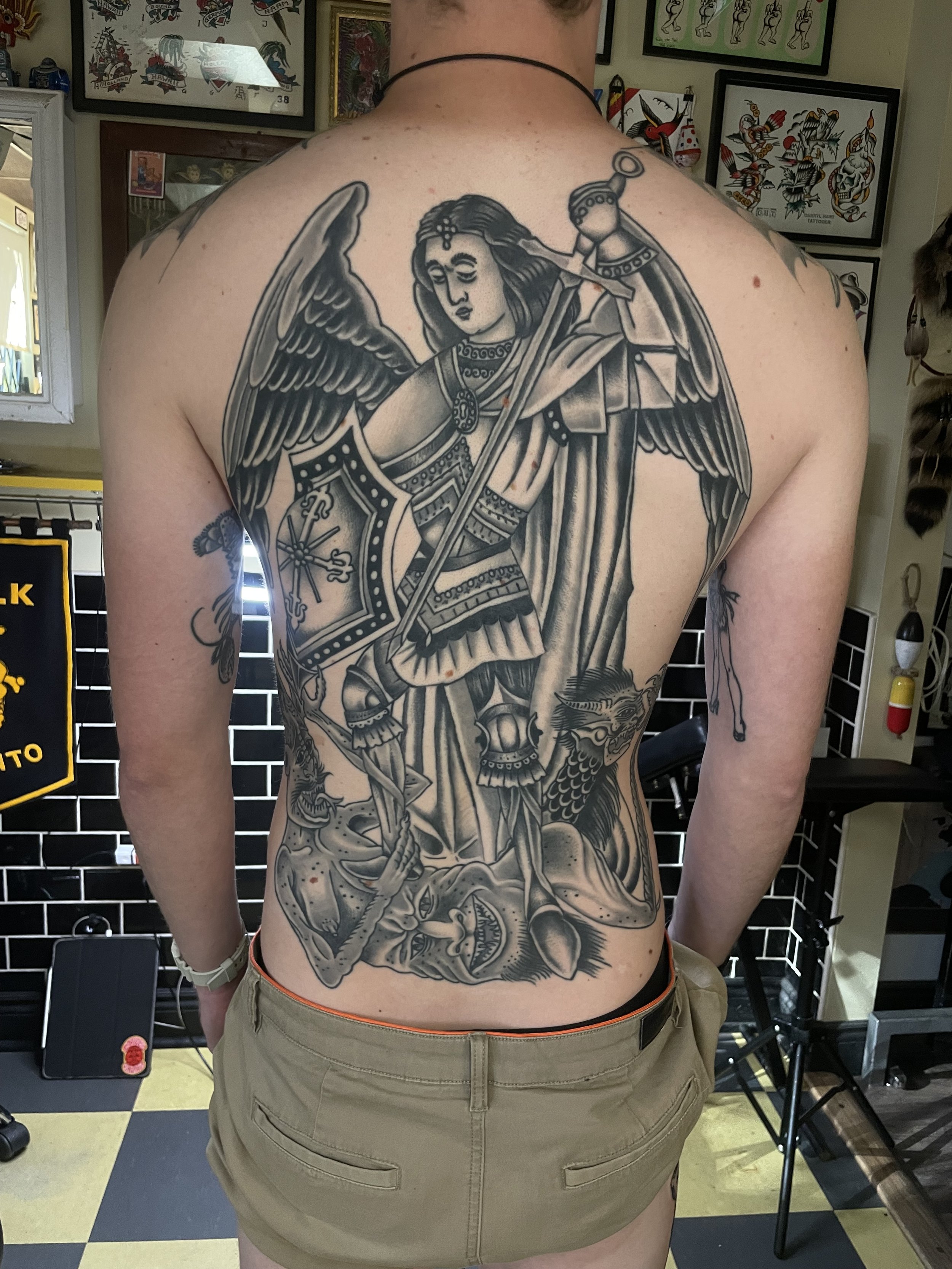 Tattoo of a warrior angel with large wings, holding a sword and shield, covering the person's back from the shoulders down to the waist.