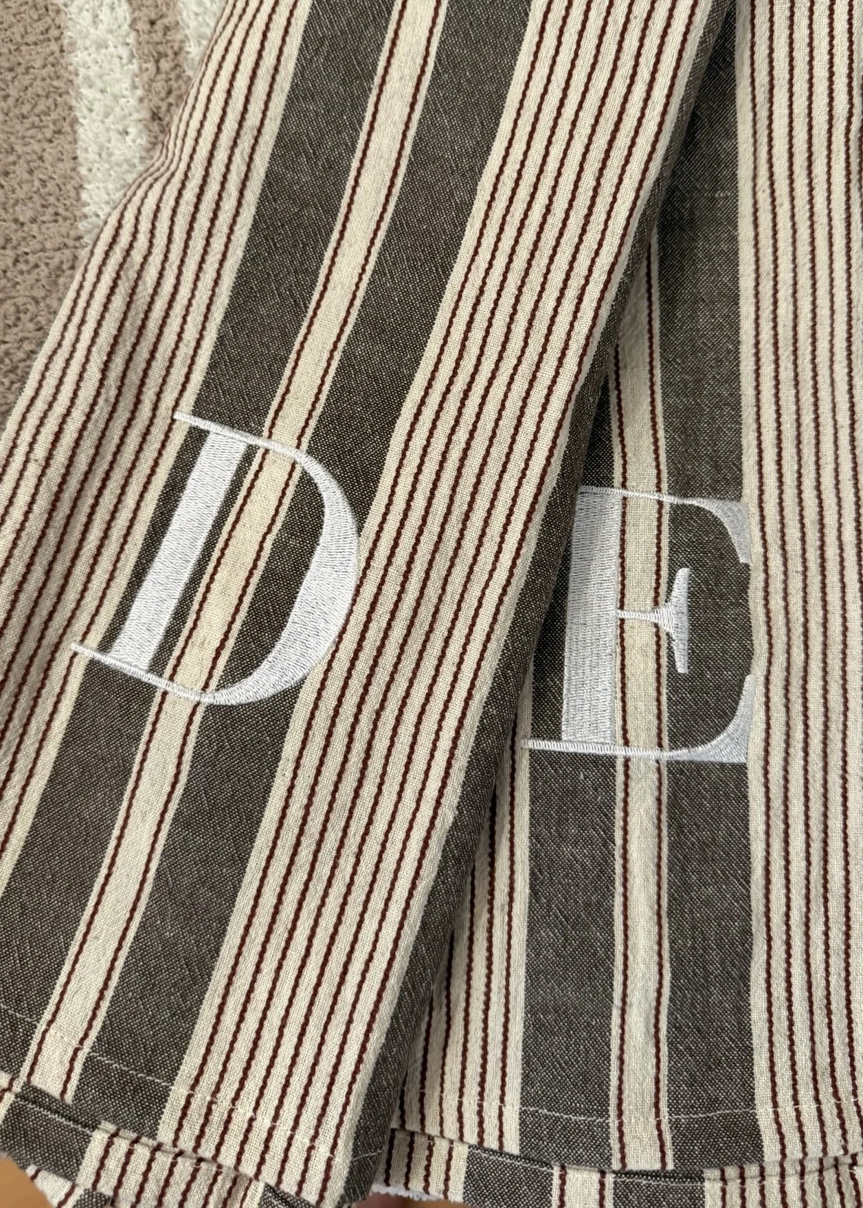 Close-up of a hand towel set with vertical white and brown stripes and embroidered white letters 'D' and 'G'.
