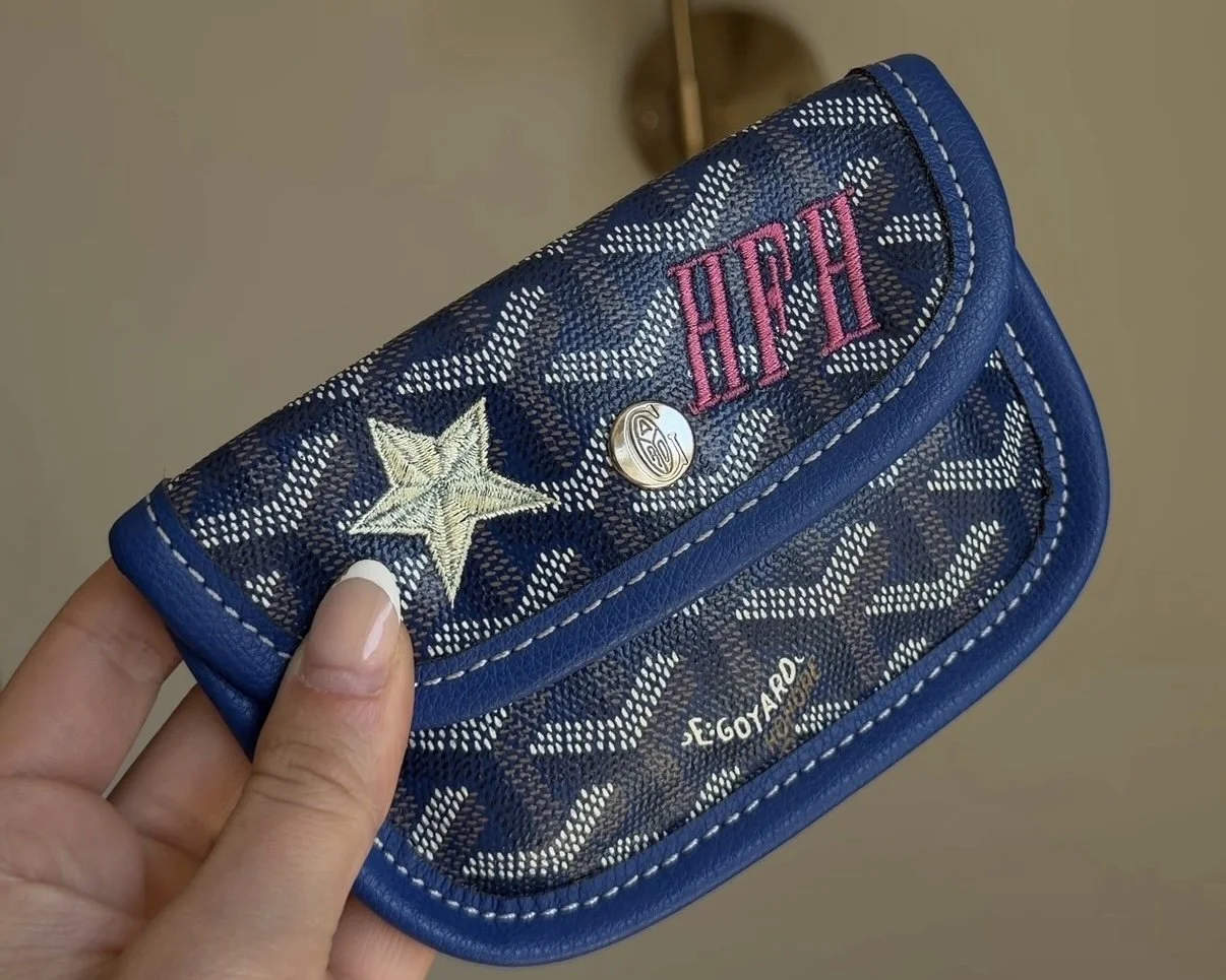 Blue designer wallet with embroidered star and pink initials.