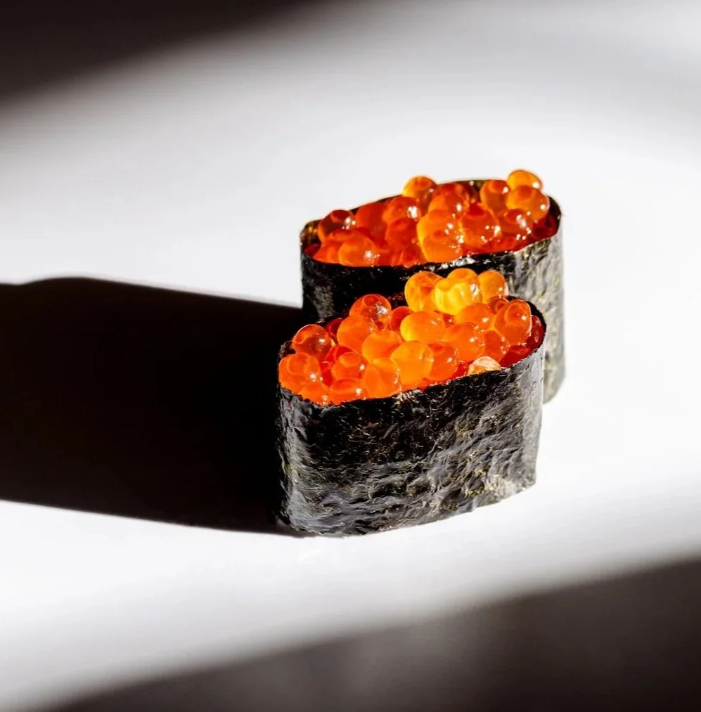 Two pieces of ikura nigiri, casting shadows on a white surface.