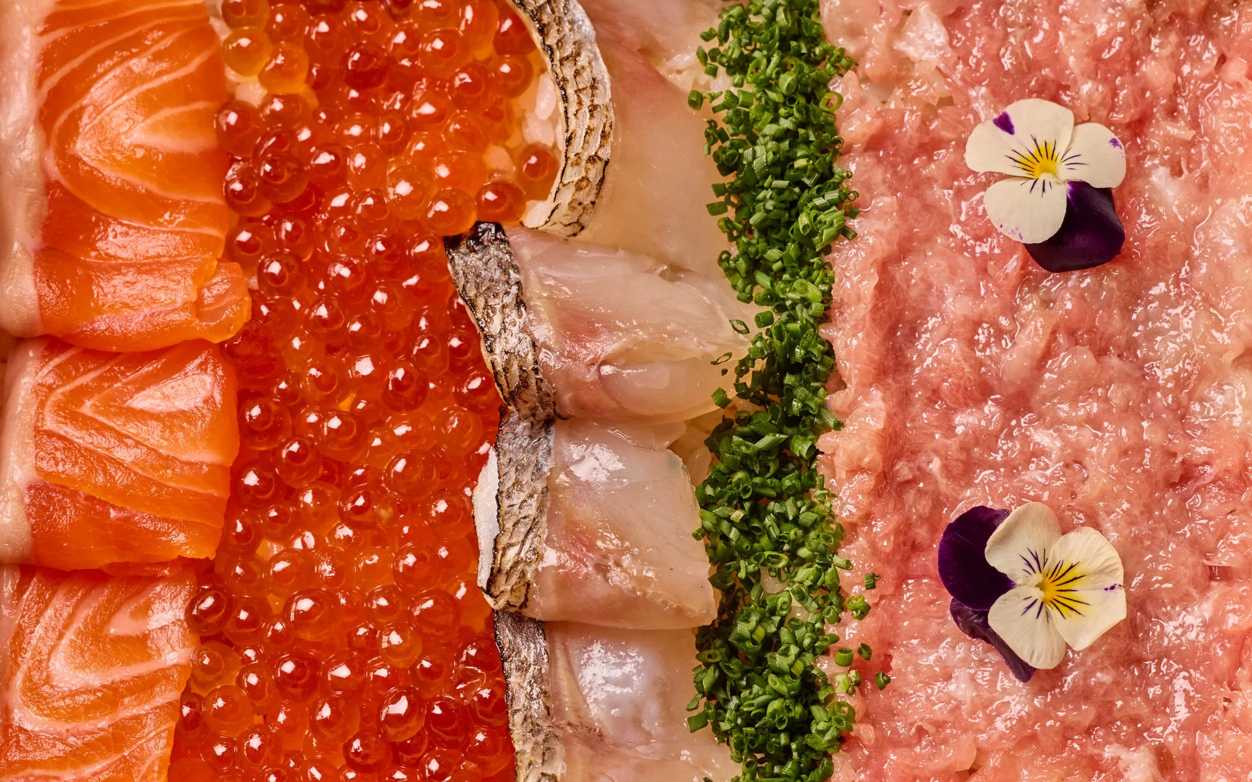 Overhead of raw fish - salmon, ikura, arctic char, chives, toro.