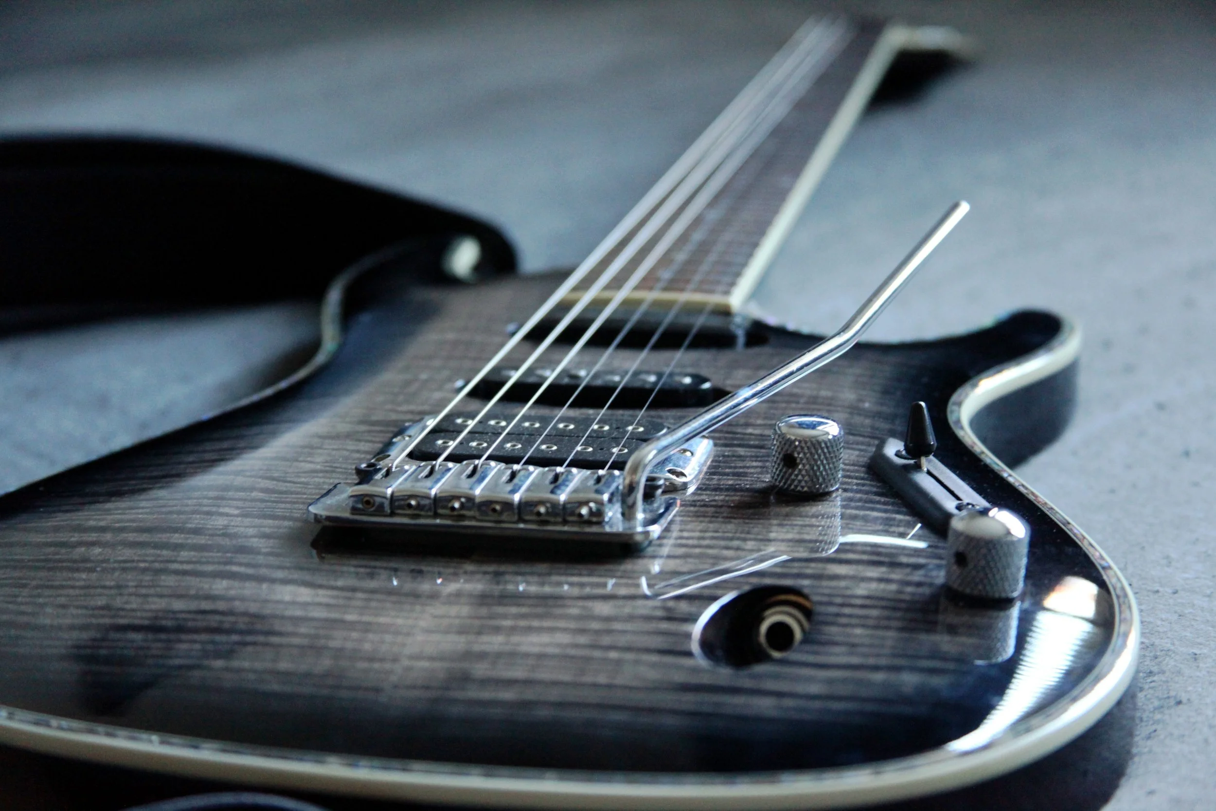Close-up of a black electric guitar lying on a surface, showing the bridge, strings, and part of the body with a metallic rim.