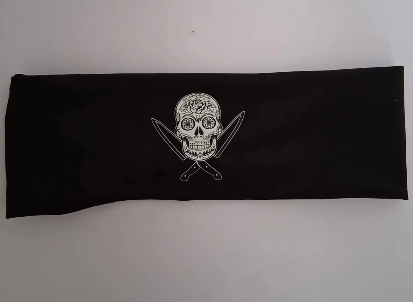 Black fabric with a white skull design, decorated with floral patterns and crossed knives below the skull.