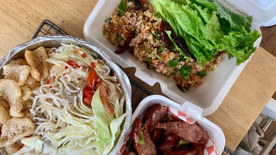 Takeout food with a vegetable and noodle salad, a breaded dish with greens, and sliced roasted meat.