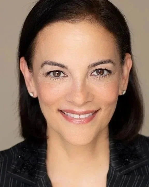 Patricia So. Close-up portrait of a smiling woman with dark hair, wearing earrings and a dark pinstripe blazer.