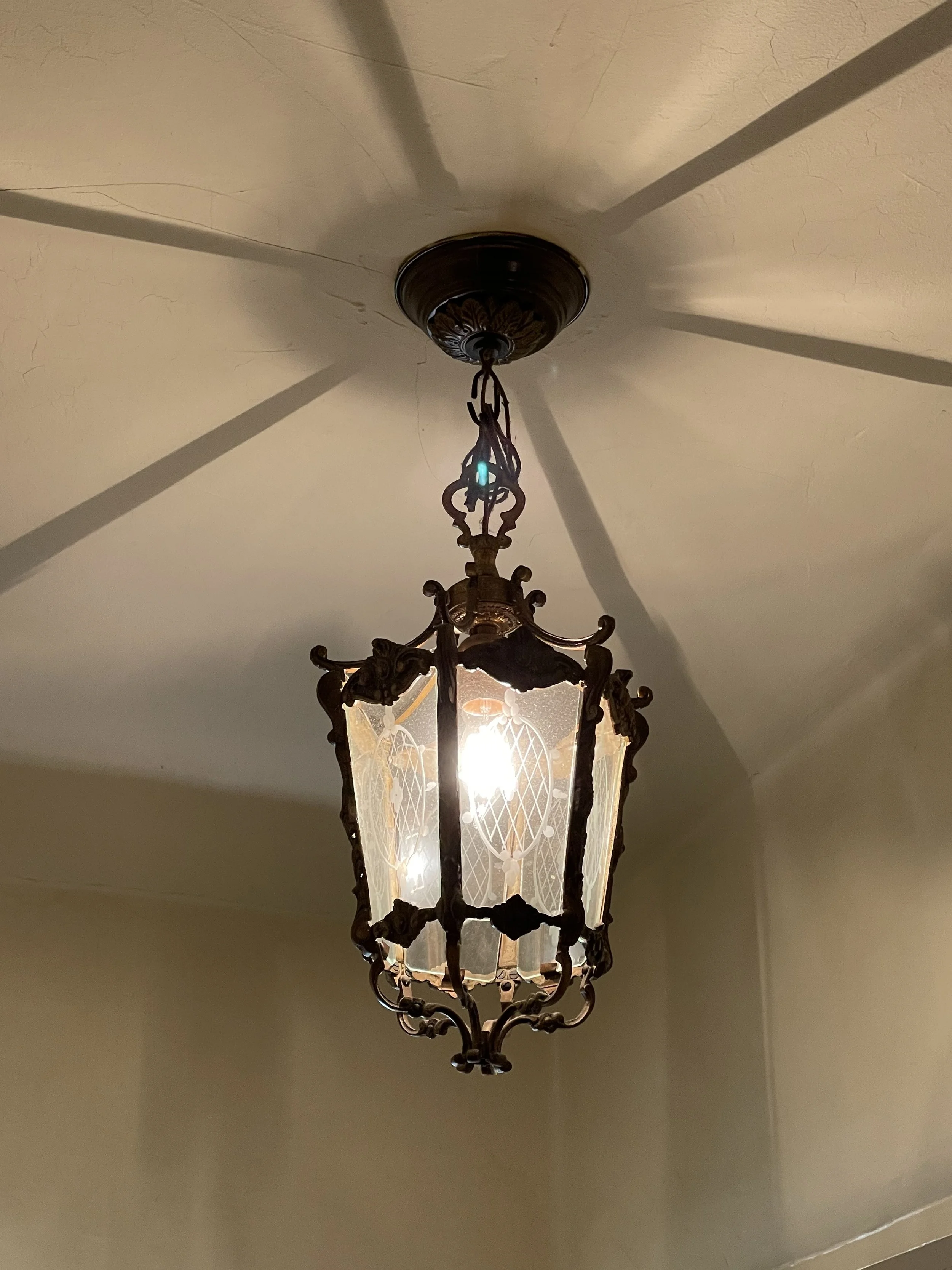 A decorative hanging lantern chandelier with an ornate metal frame, glass panels, and a light bulb inside, hanging from a ceiling at a home in Silver Lake.