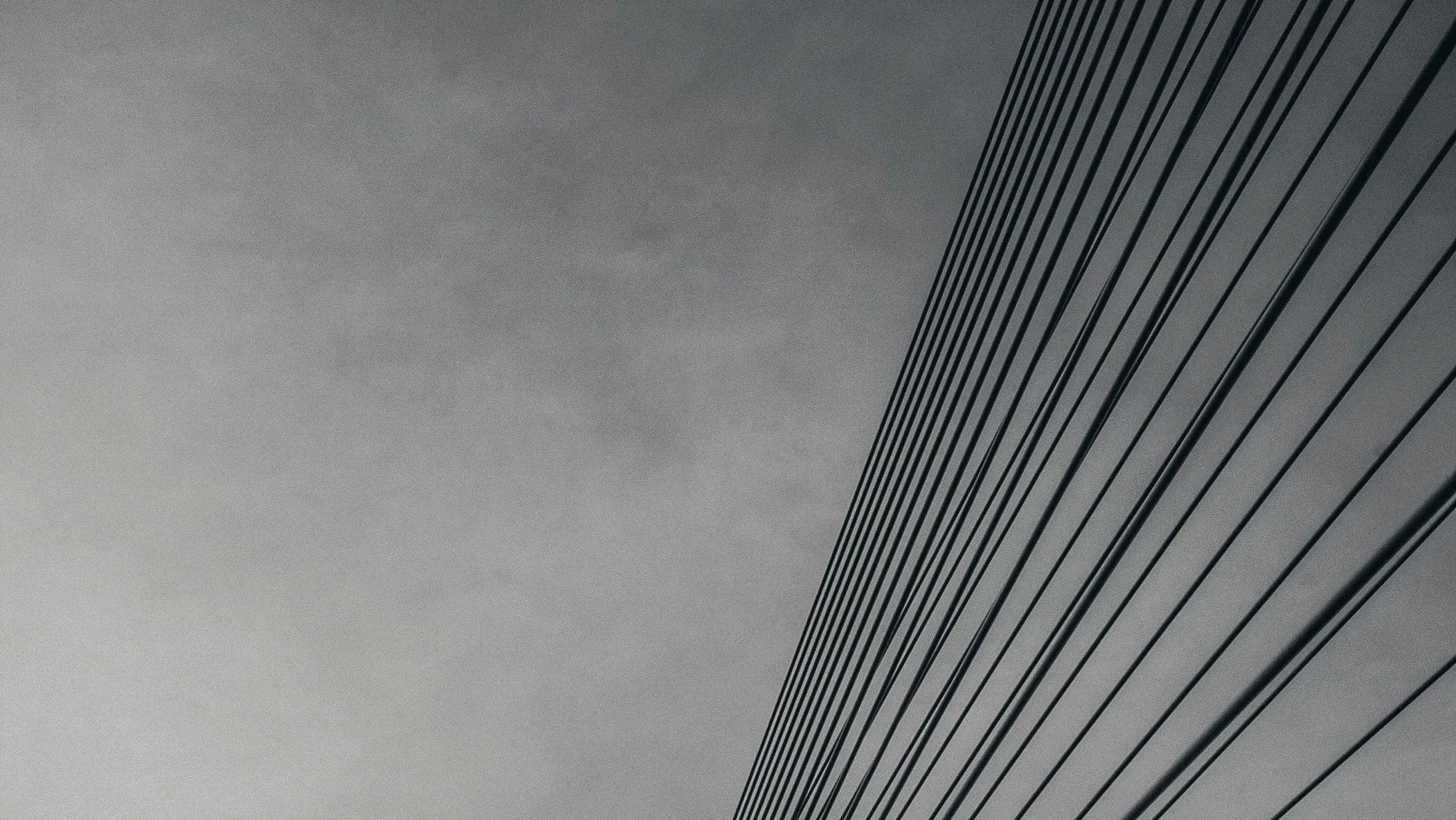 Close-up of a modern building's exterior with diagonal lines and a cloudy sky in the background.