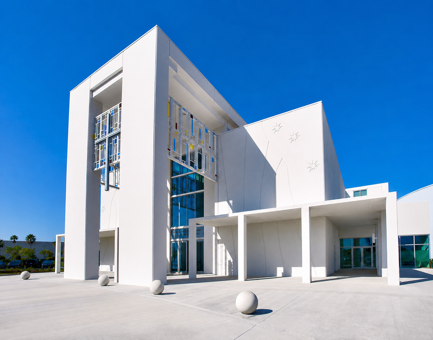 Modern white building with geometric design, large glass windows, and decorative window panels under a clear blue sky.