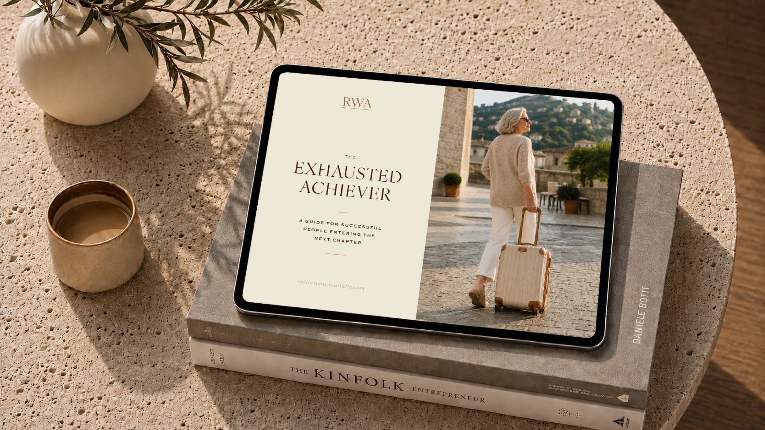 A tablet displaying a book cover titled 'The Exhausted Achiever' with a woman in a beige coat and white pants carrying a rolling suitcase in a scenic outdoor setting. The tablet is on top of two books and a lace tablecloth, with a white vase with green leaves and a cup of coffee nearby.