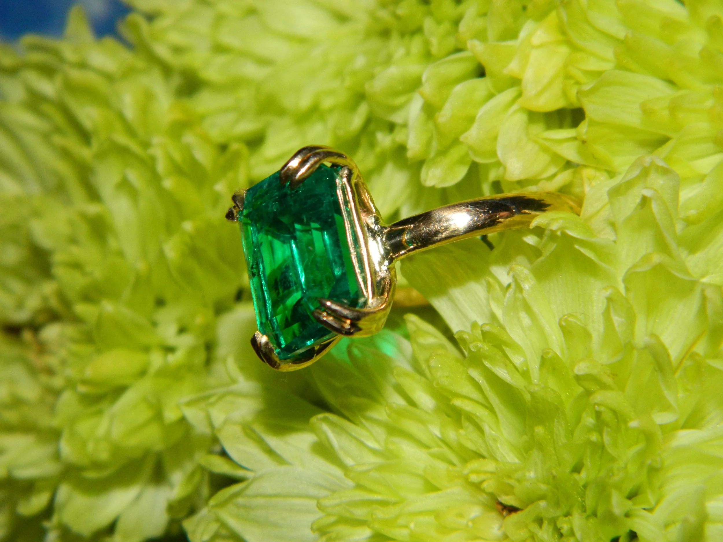 A close-up of a small metallic green gemstone ring on a bright green textured surface.