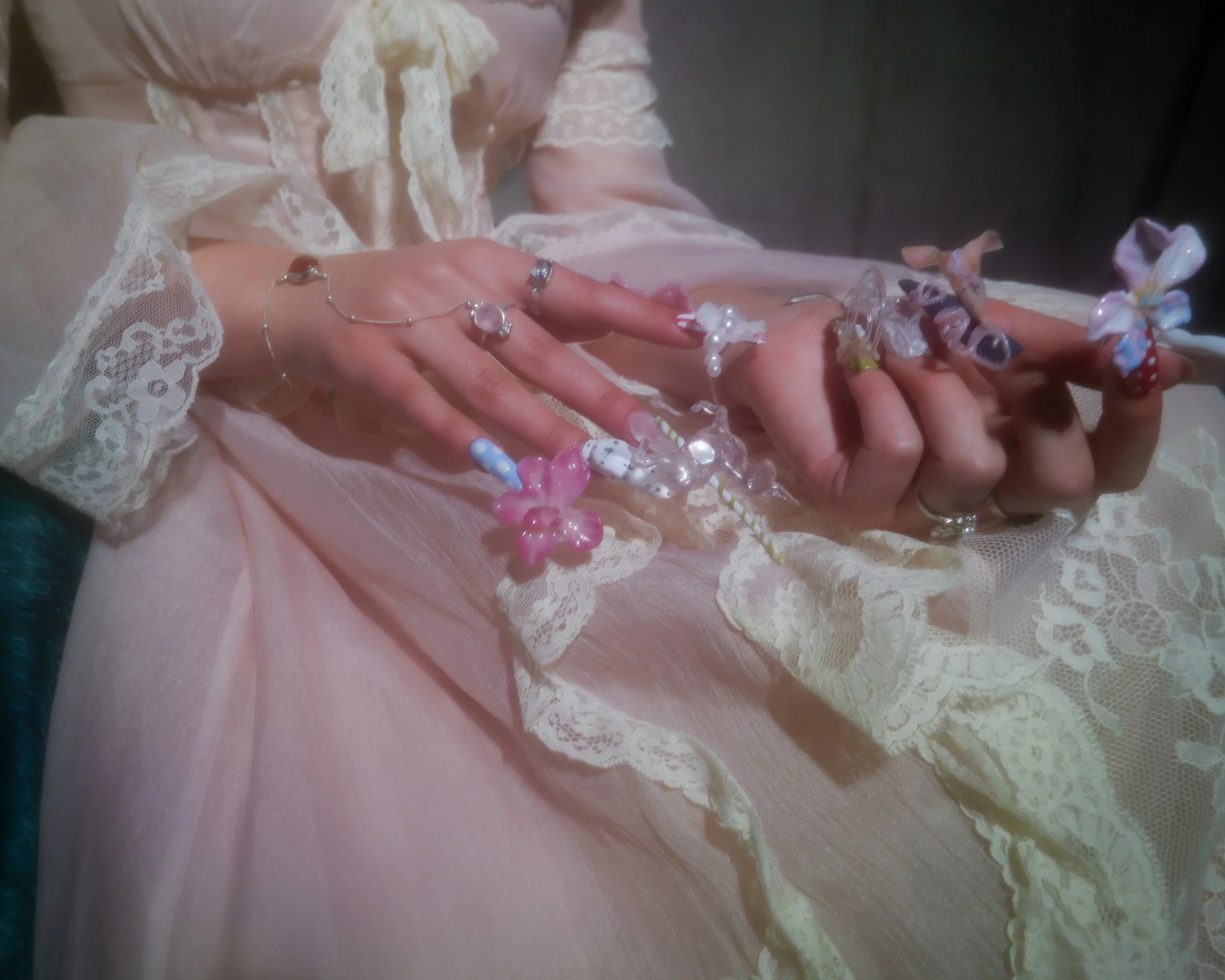 Close-up of a person's hands resting on a pink lace dress, decorated with colorful candy-shaped accessories and jewelry.