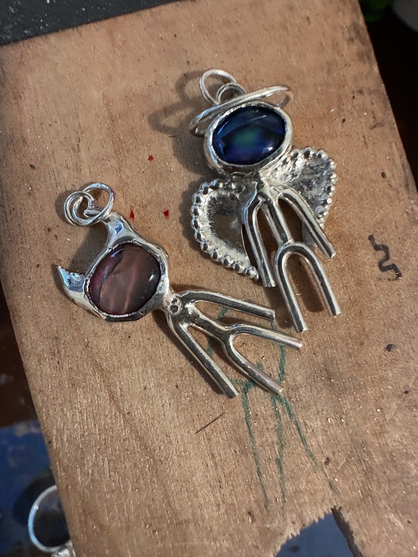 Silver jewelry pieces with dark blue, pink, and black stones on a wooden surface.