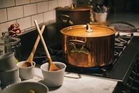 A kitchen stove with a large copper pot, a saucepan, and some cooking utensils on the countertop.