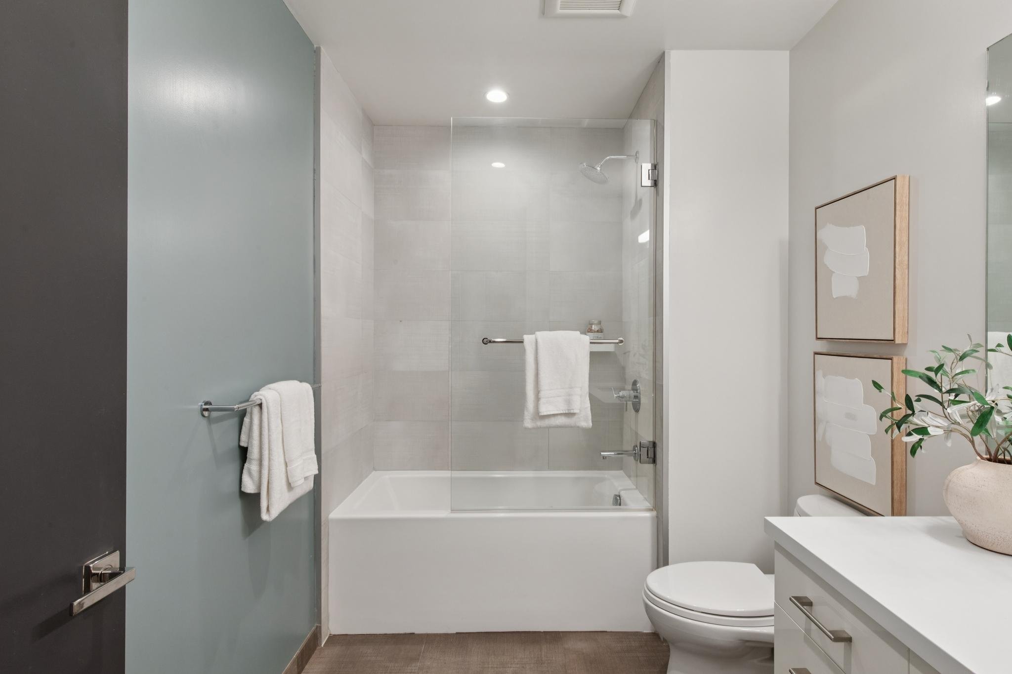Modern bathroom with walk-in shower, white walls, a toilet, and decorative artwork on the wall.