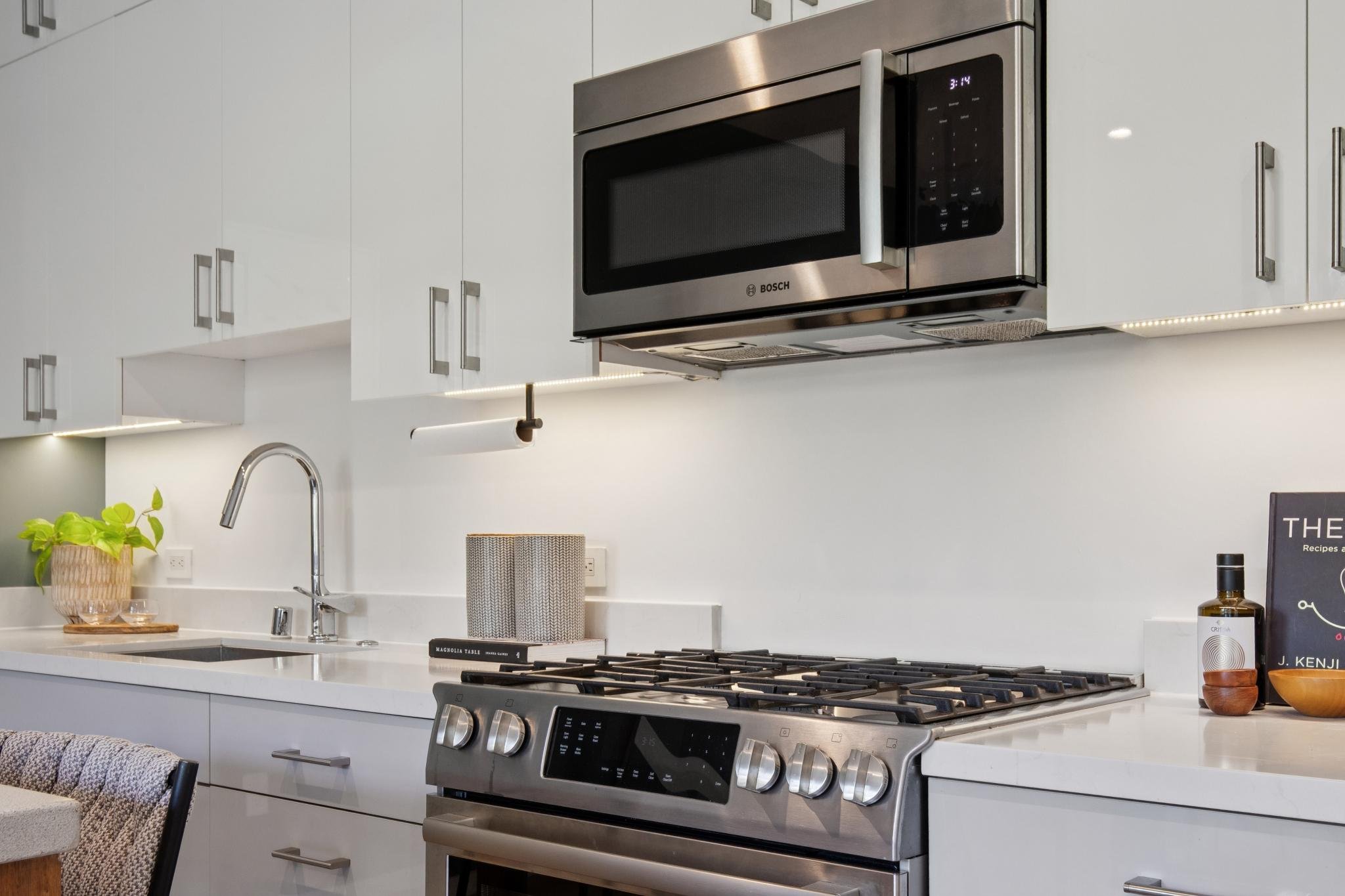 Modern kitchen with white cabinets, stainless steel microwave, gas stove, white countertop, plant, and decorative items.