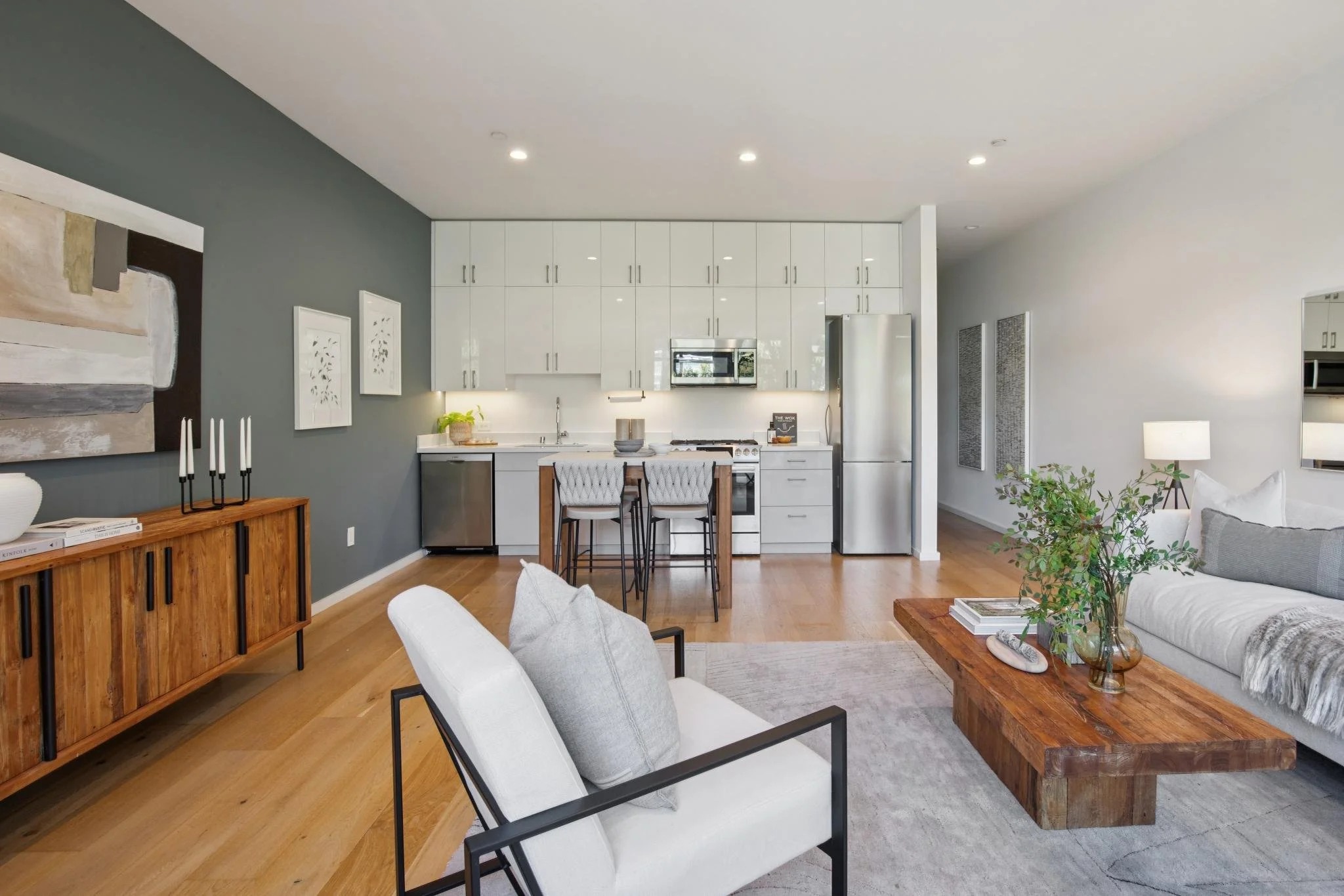 Modern open-concept living room and kitchen with gray walls, white cabinetry, wooden furniture, and minimalist decor.