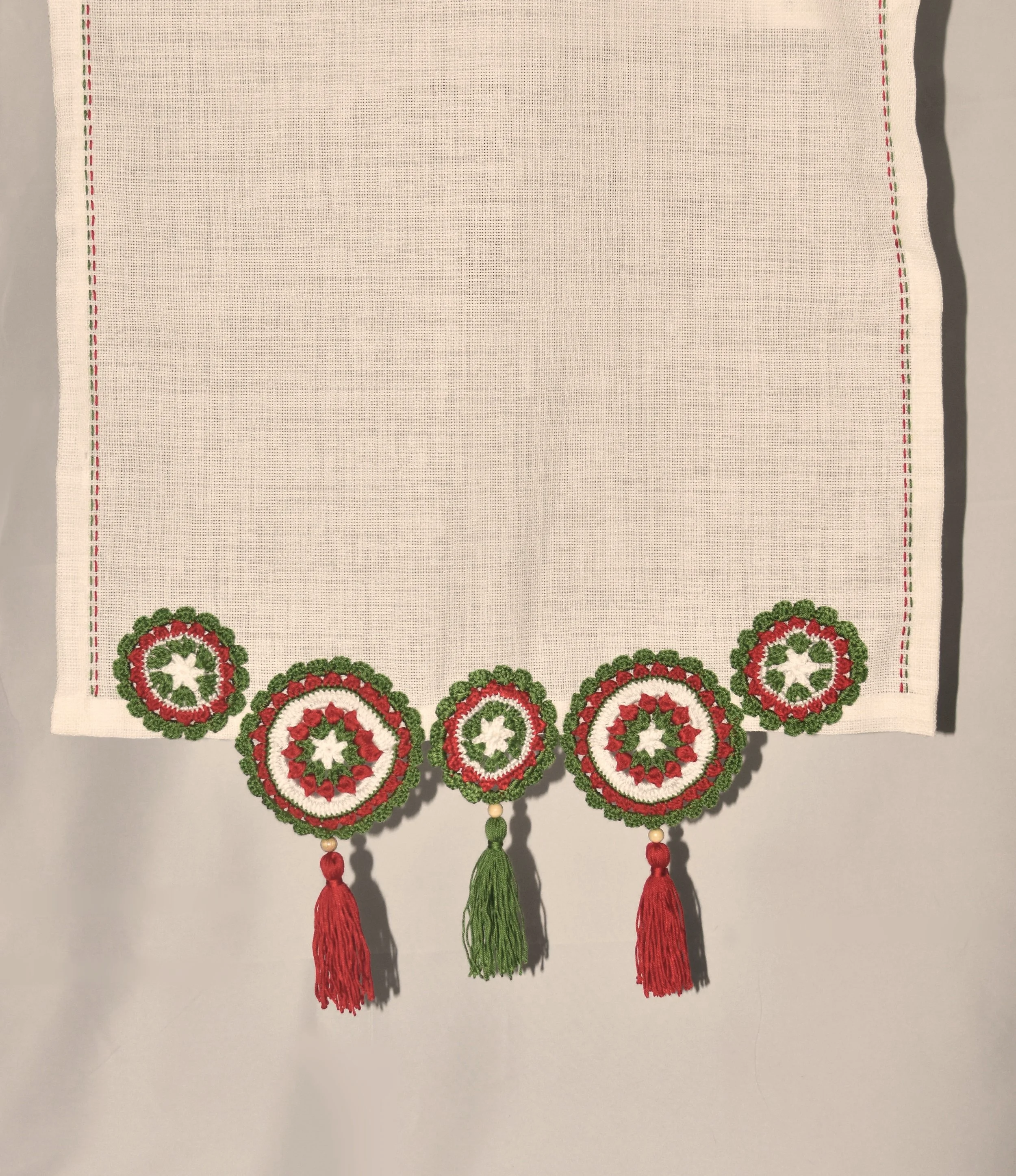 A decorative embroidery piece with a pattern of red, white, and green circles at the bottom, wearing red and green tassels, on a white fabric background.