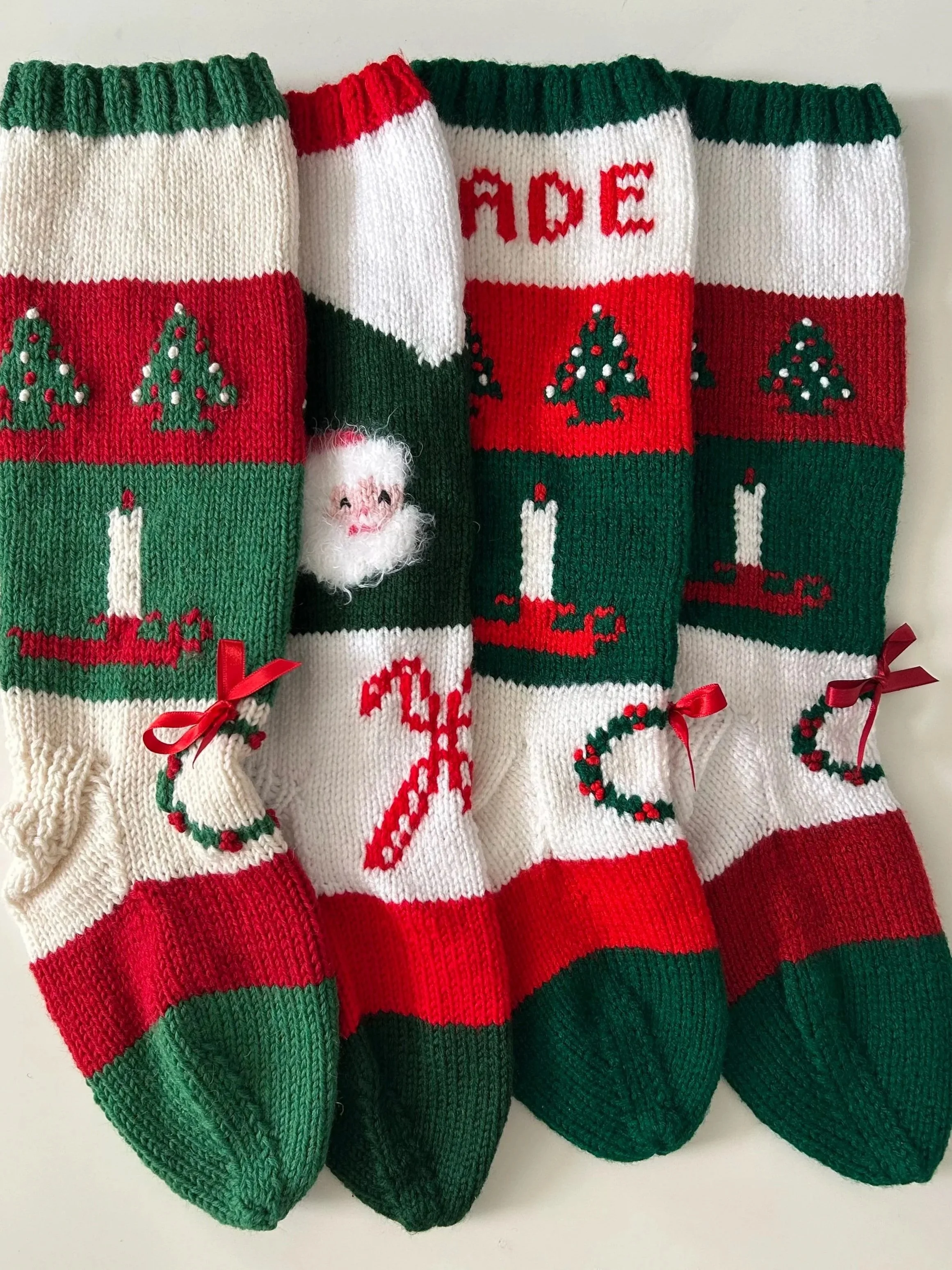 Set of four Christmas stockings with red, green, and white yarn, decorated with Christmas trees, a candle, and the red letters 'NOEL'.