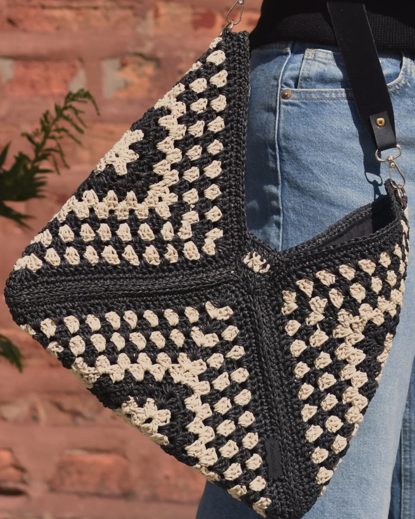 Close-up of a black and beige crocheted or woven bag hanging near a person's waist, with part of their blue jeans visible.