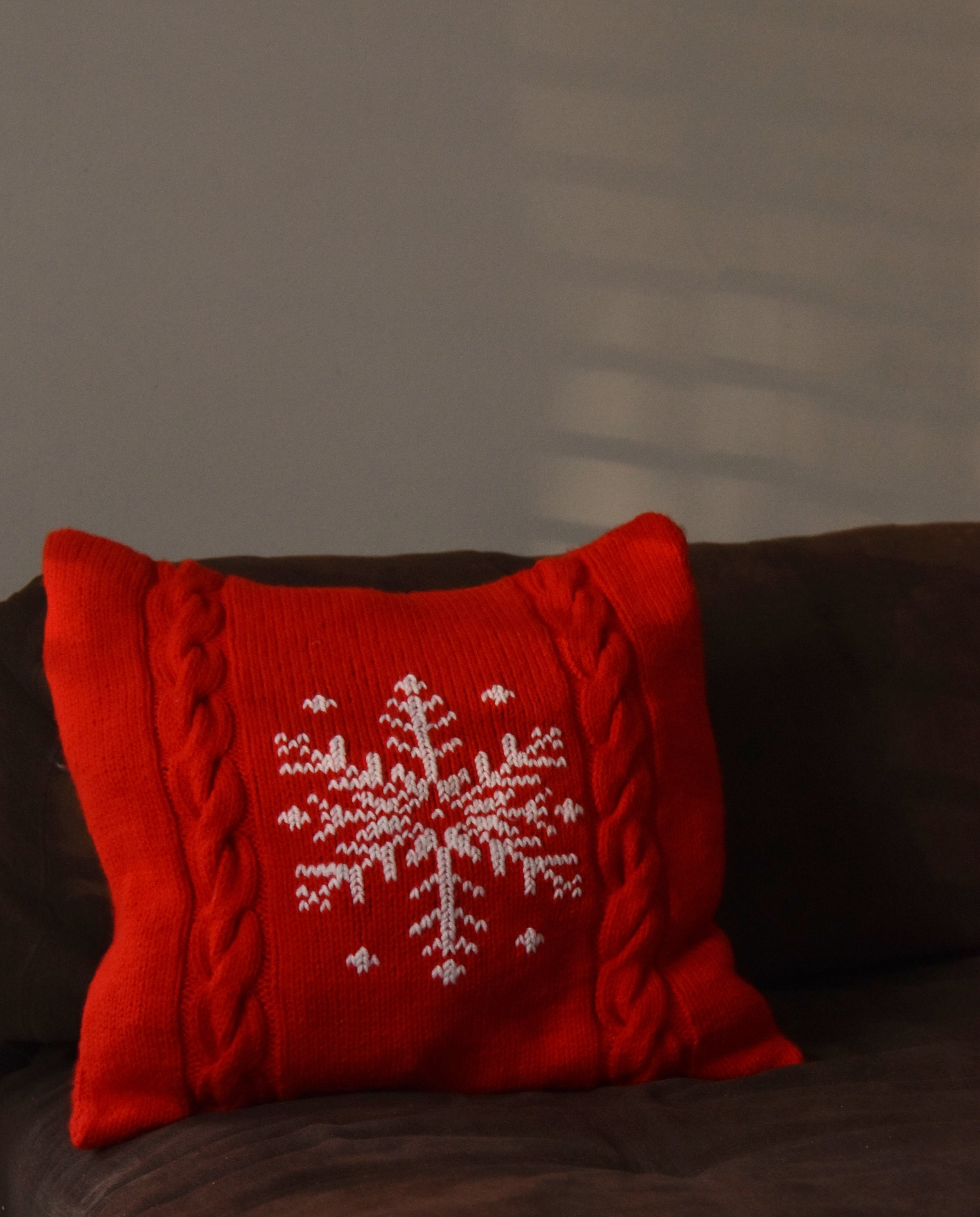 Close-up of a red holiday sweater with white reindeer and snowflake pattern, placed on a dark surface.