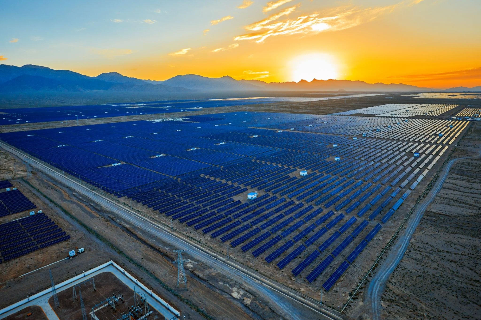 A large solar farm with rows of solar panels at sunrise near mountain ranges.