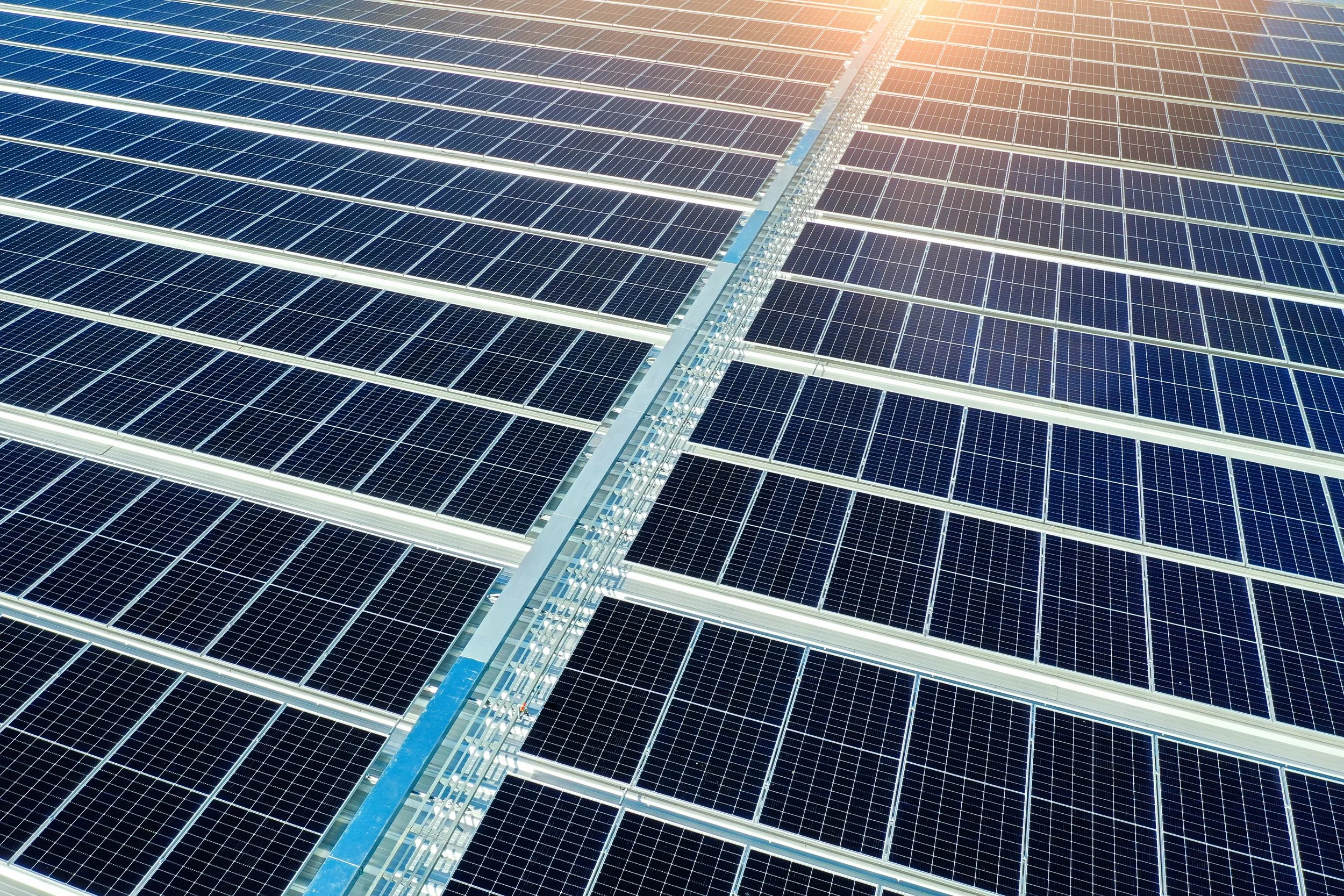 A large array of solar panels installed on a rooftop or field, with sunlight shining down on them.