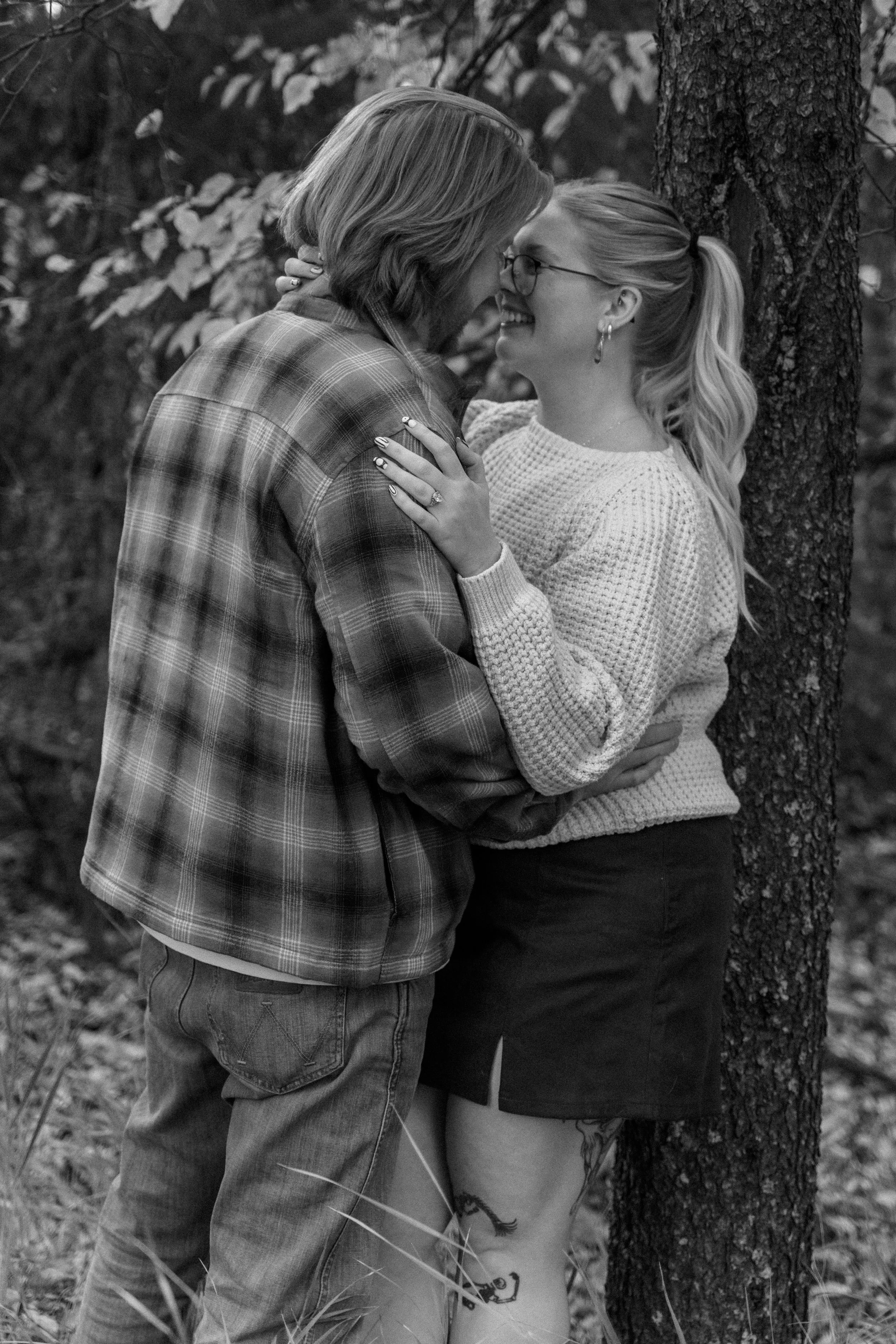 Black-and-white outdoor portrait of two women embracing and smiling beside a tree.