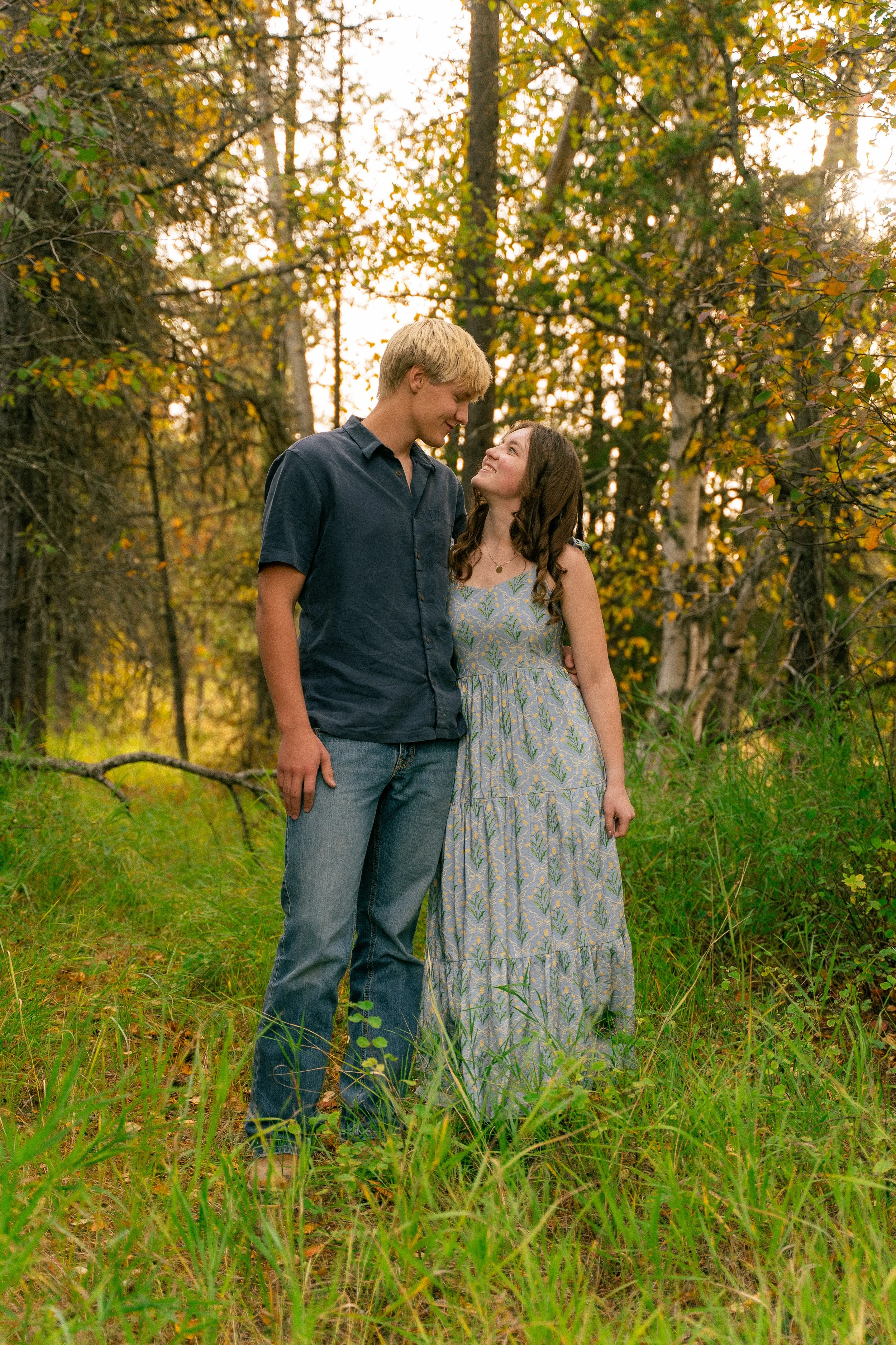 Young couple smiling at each other in a sunlit autumn forest
