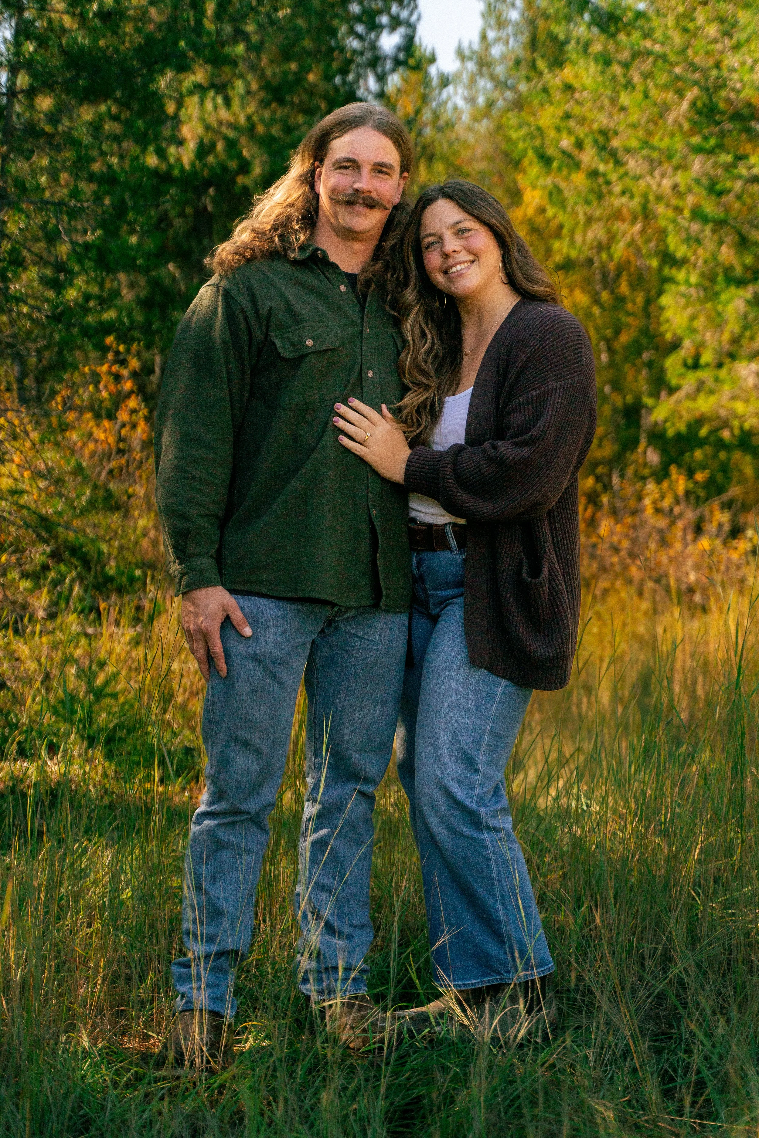 Smiling couple embracing in a sunlit grassy field surrounded by autumn trees