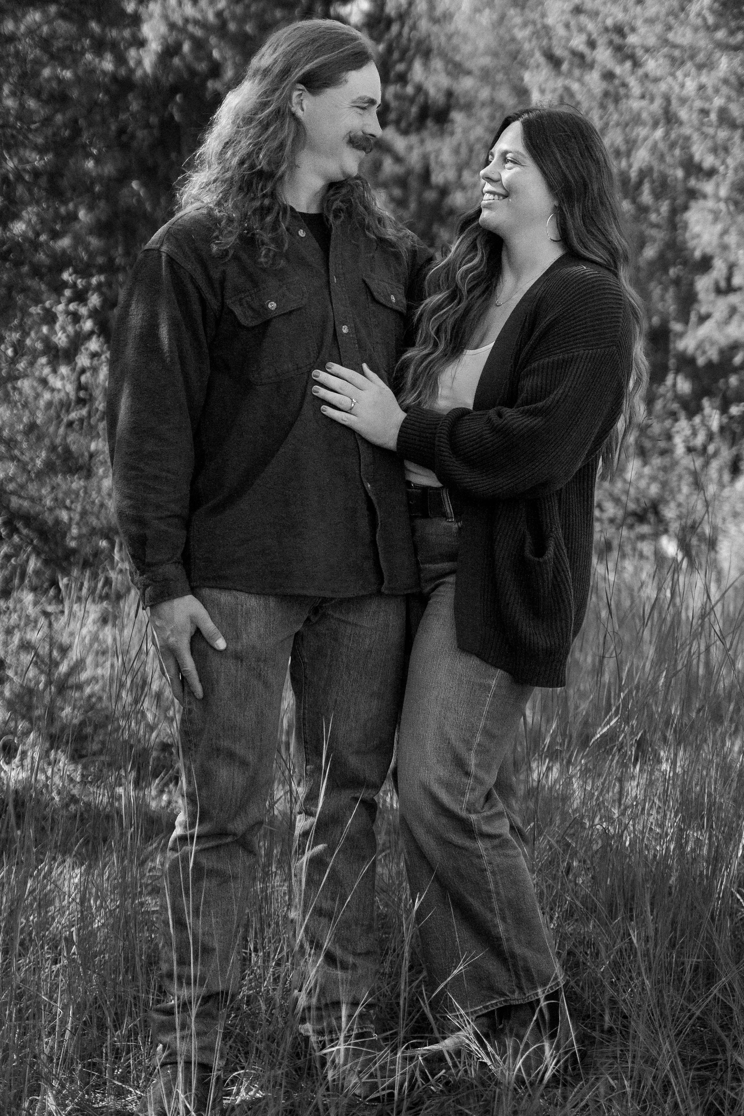 Black-and-white portrait of a smiling couple embracing in a grassy field