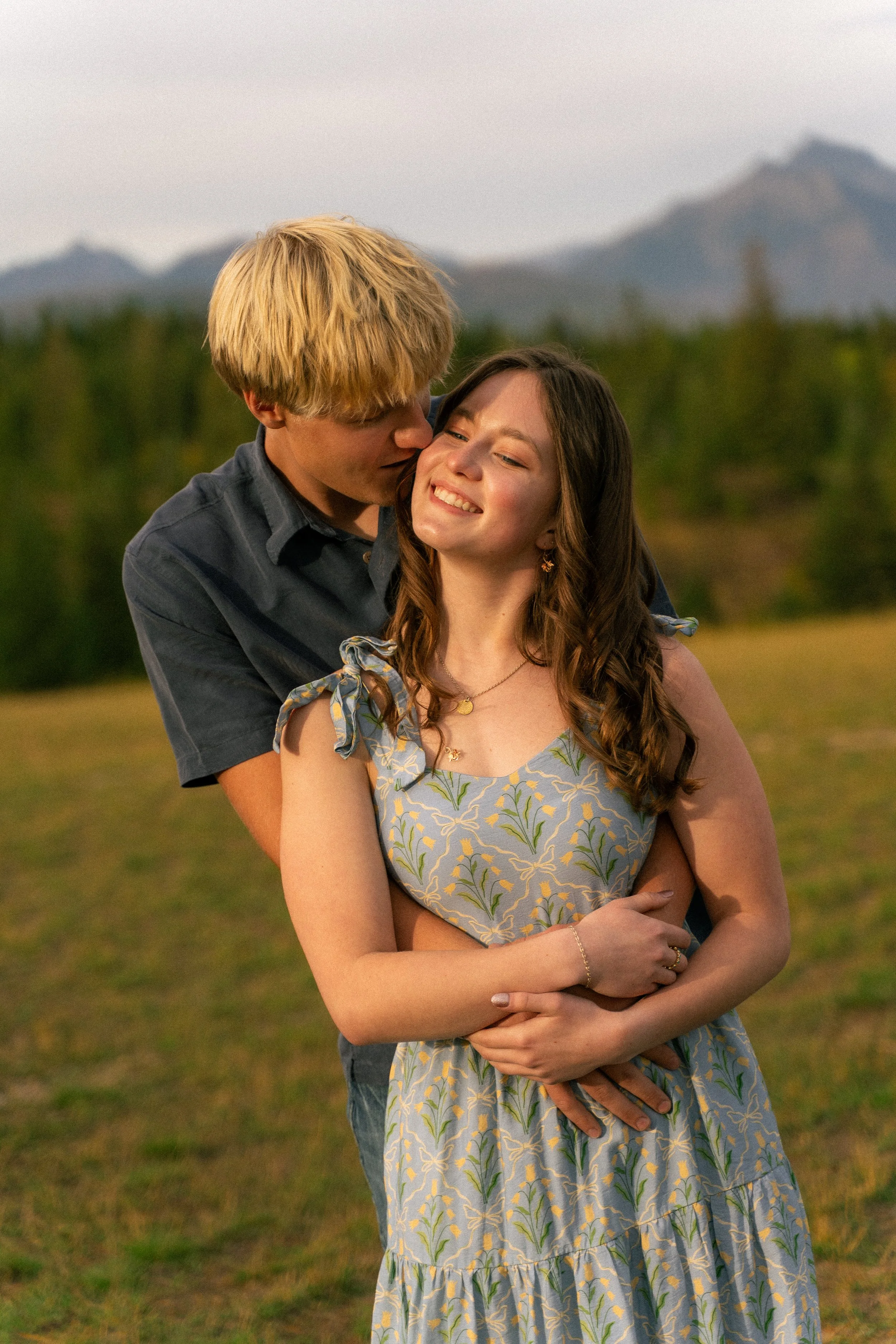 Smiling couple embracing outdoors as the man kisses the woman's cheek in a sunlit field
