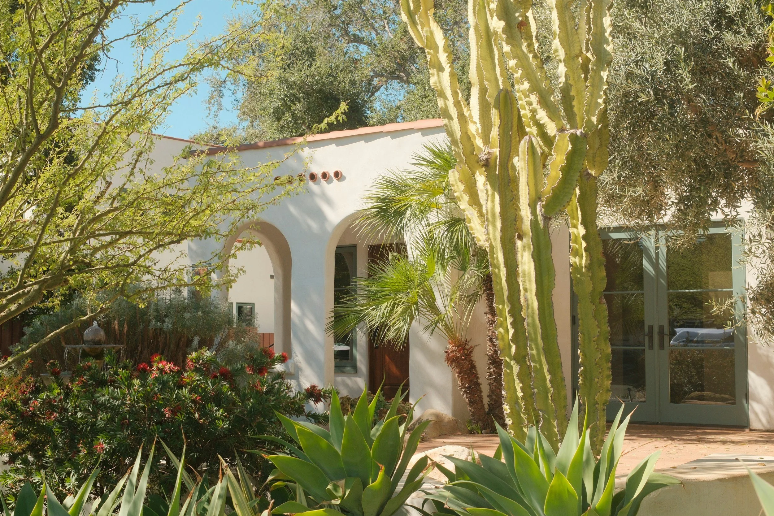 White stucco Spanish-style home with a clay tile roof, surrounded by drought-tolerant agave, cactus and palms