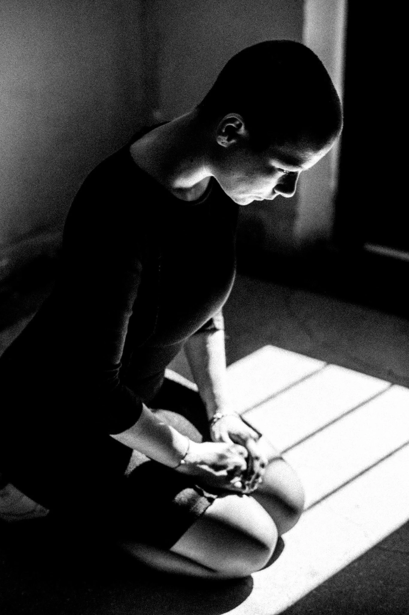 A black-and-white photo of a person sitting on a bench, looking down, with a focused or thoughtful expression.