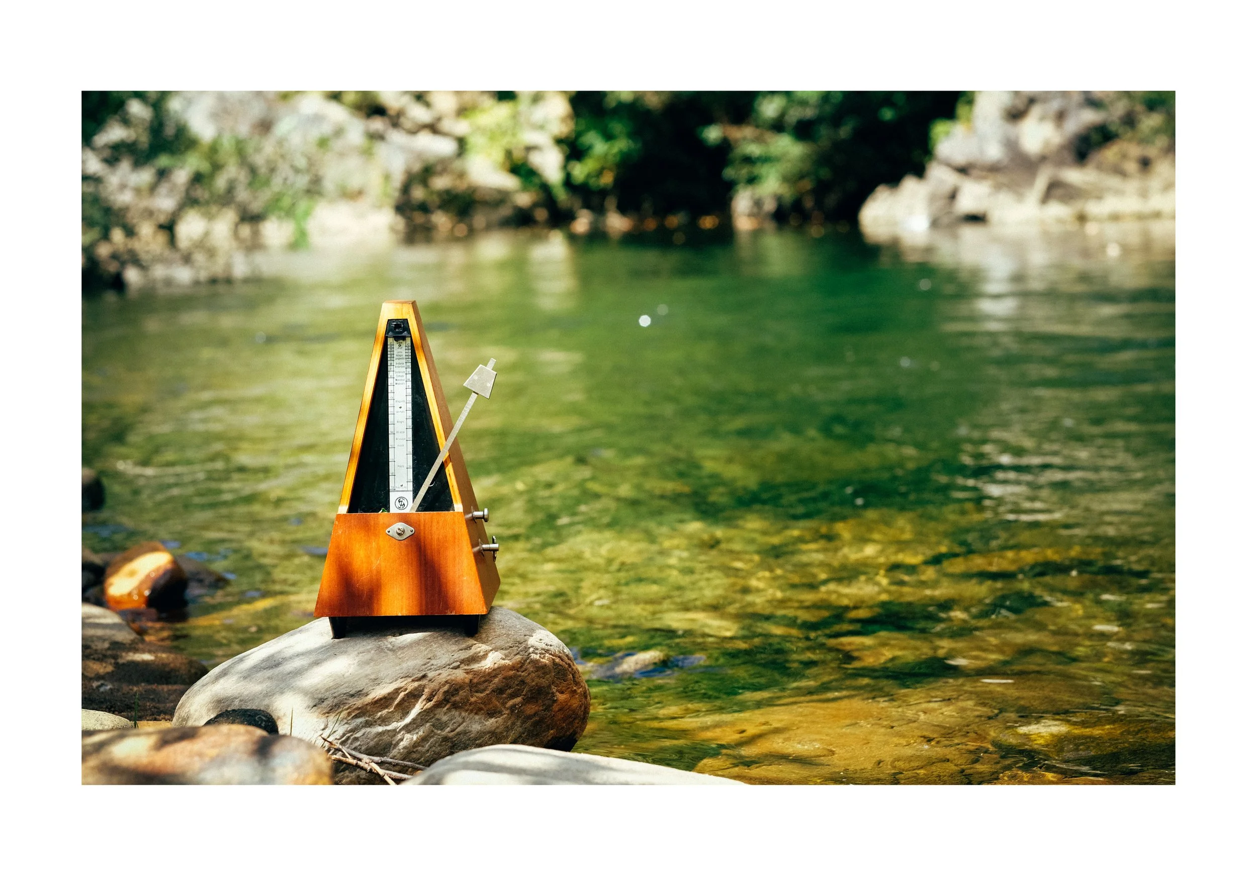 A wooden river flow meter placed on rocks in a river with clear water and a forested background.