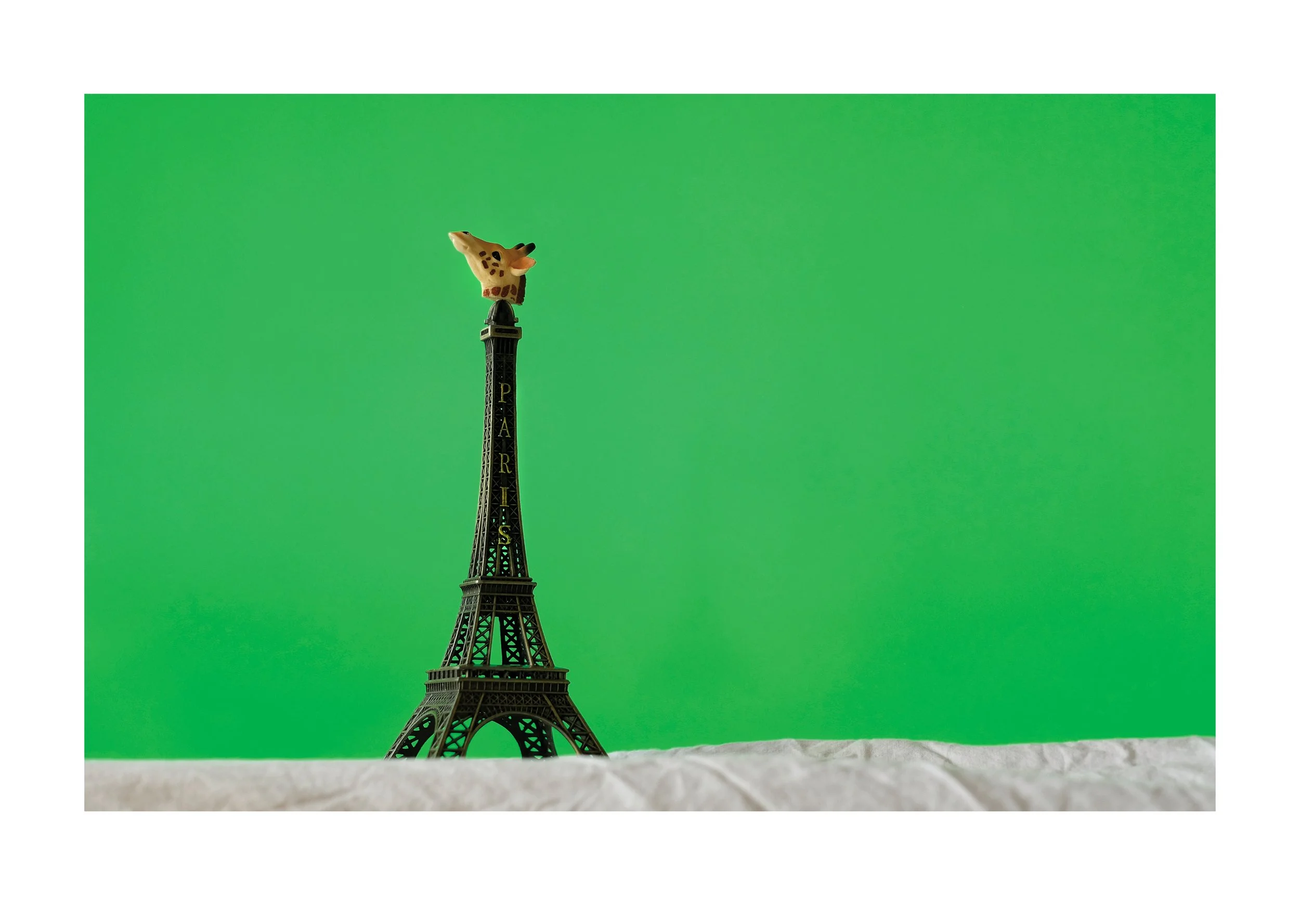 Small giraffe figurine on top of an Eiffel Tower souvenir replica with a green background.