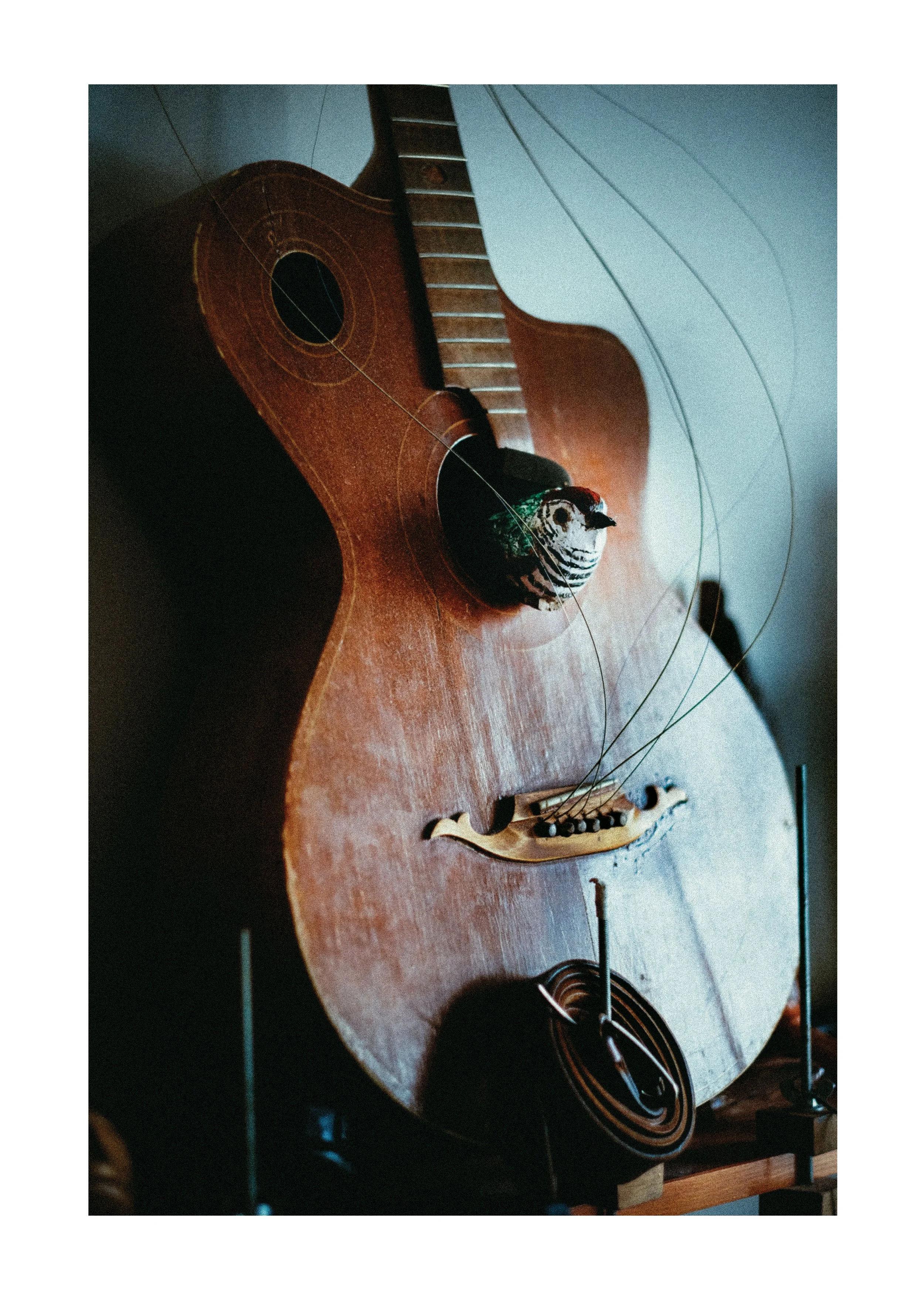 A wooden acoustic guitar with visible strings, resting on a table. There is a small bird figurine or toy near the guitar and other objects on the table.
