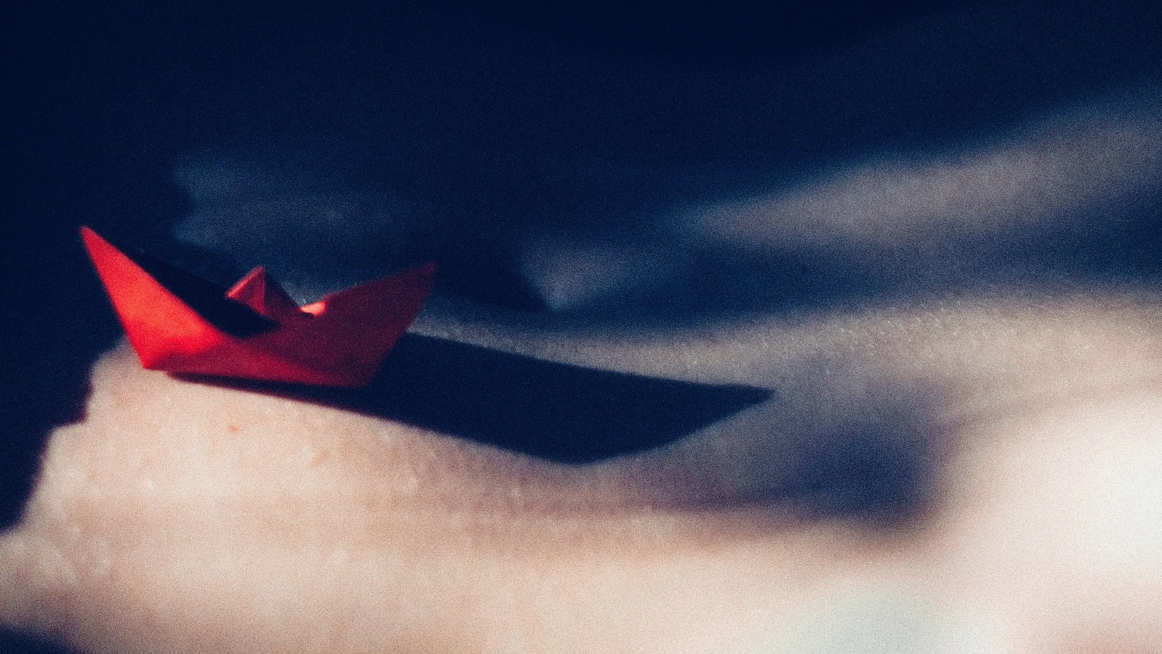 A small red paper airplane resting on a light-colored surface with a dark background.