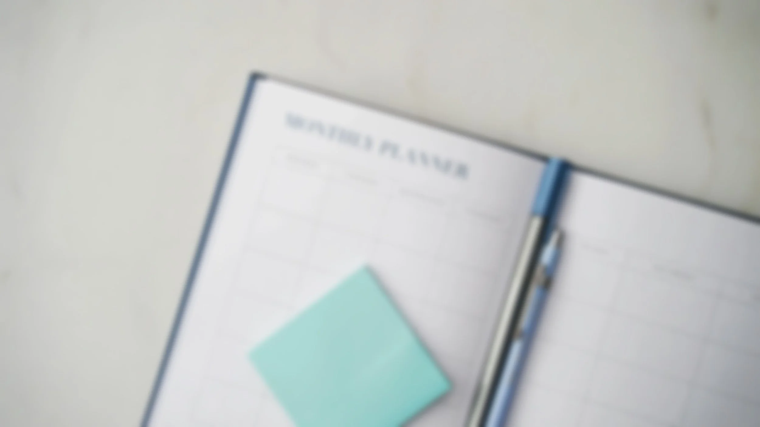 Close-up of a notebook with a book titled 'BUSINESS PLANNING' on a light-colored surface.