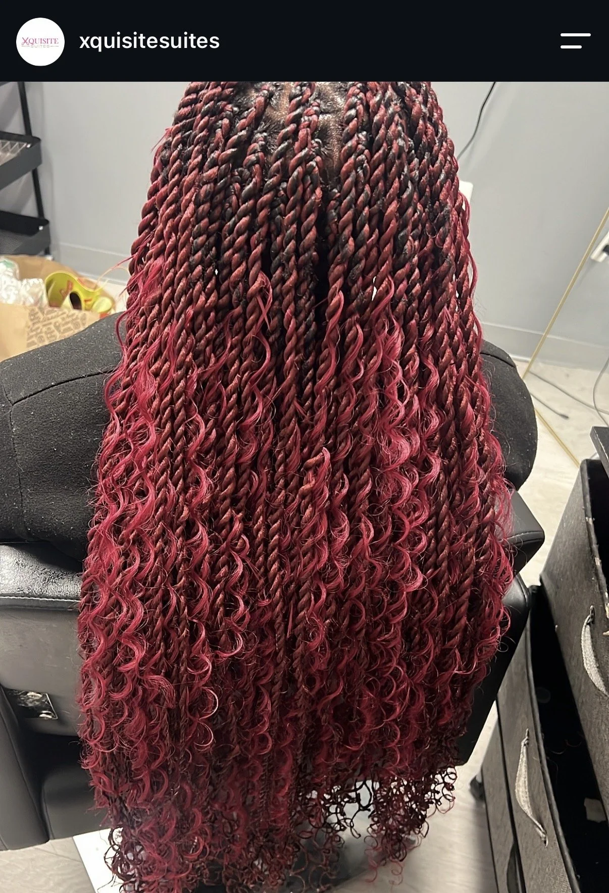 Back view of a woman with long, red and black braid-style hair, styled with tight twists that transition into curls at the ends.