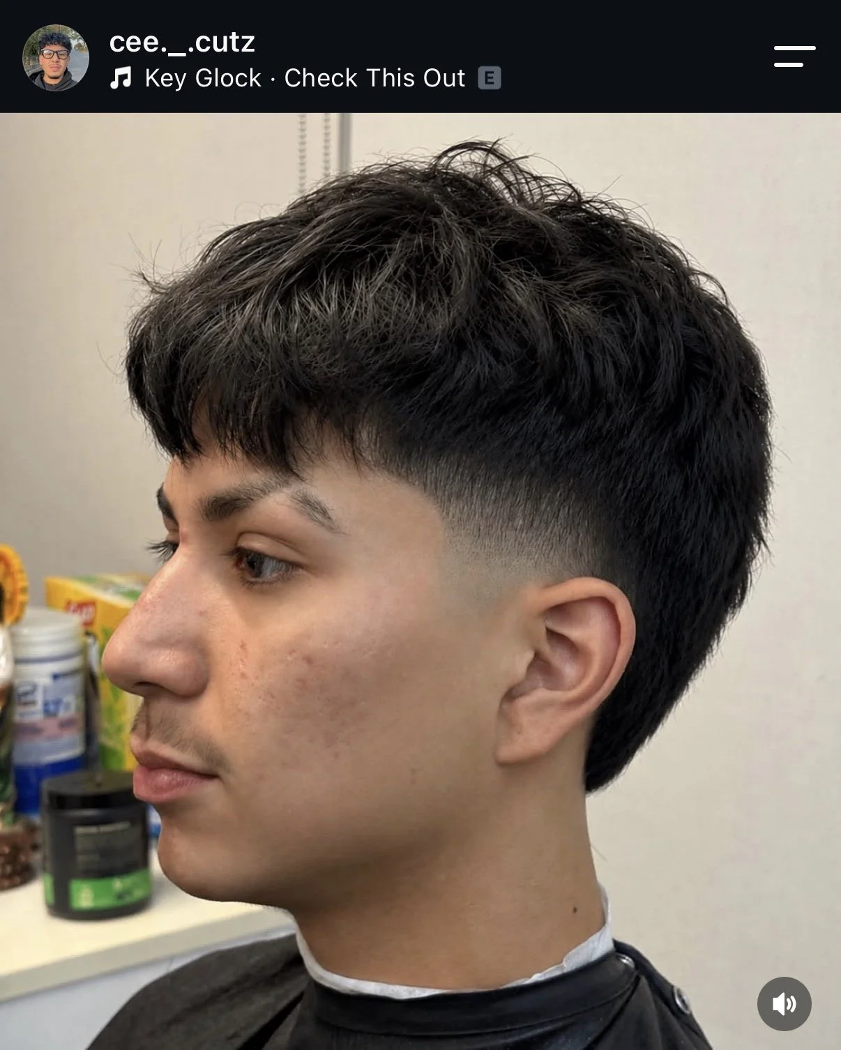 Side profile of a young man with a haircut featuring a faded undercut and curly hair on top, sitting in a barbershop.